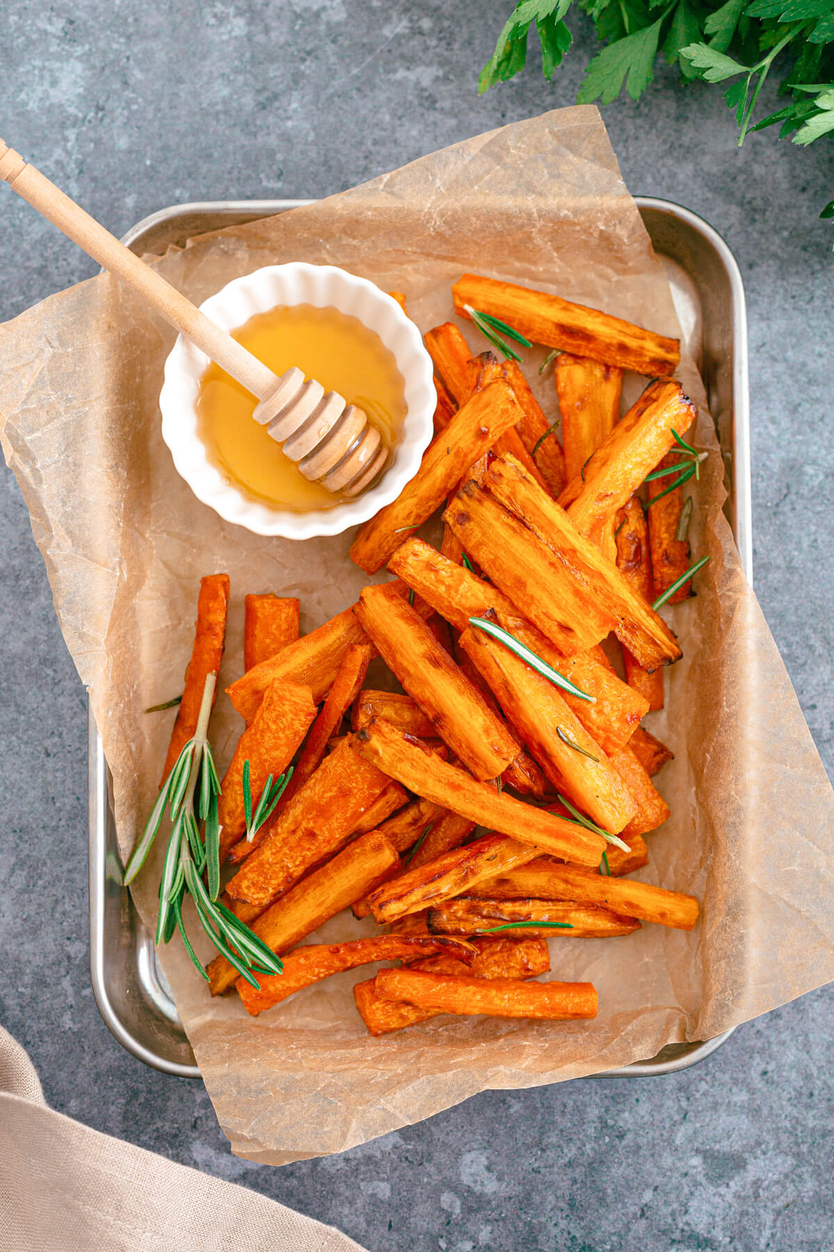 Perfectly roasted air fryer carrots on a parchment lined tray with rosemary and a small dish of honey. 
