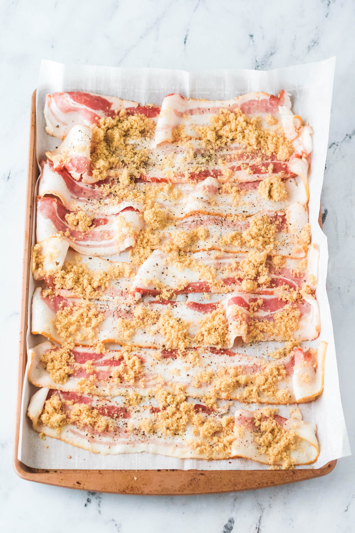 Strips of bacon covered in brown sugar on a baking sheet.