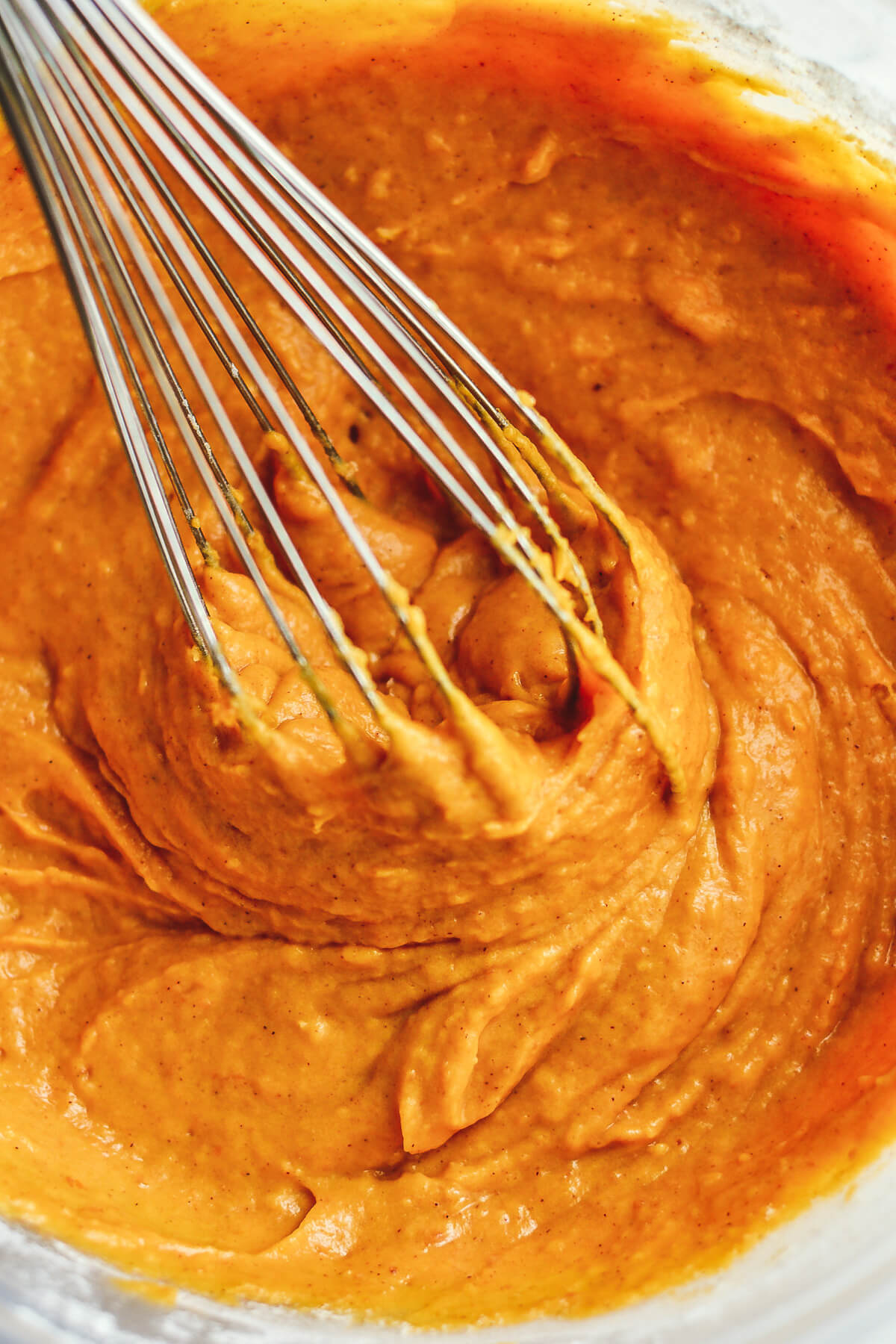 A whisk in a mixing bowl filled with orange pumpkin coffee cake batter.