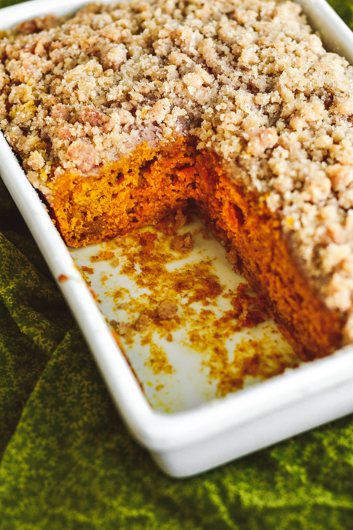 Baked pumpkin coffee cake topped with golden streusel in a white baking dish with one corner removed.