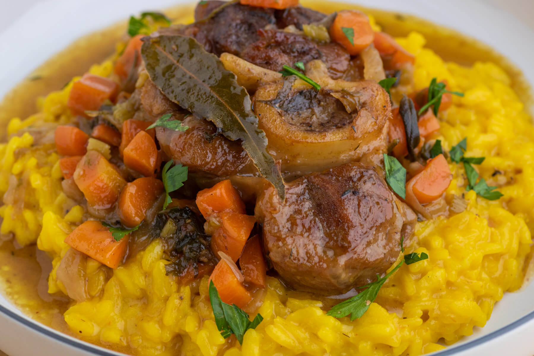 A slow cooked veal Osso Bucco served on top of vibrant yellow bed of saffron risotto Milanese.