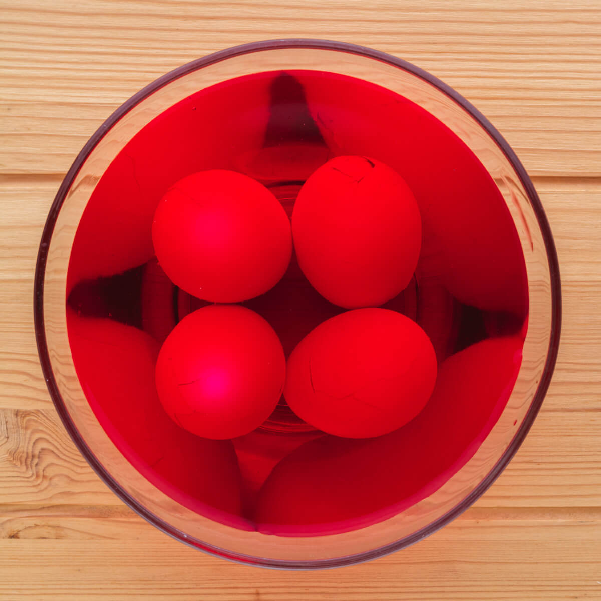 Cracked eggs in a bowl of red dye.