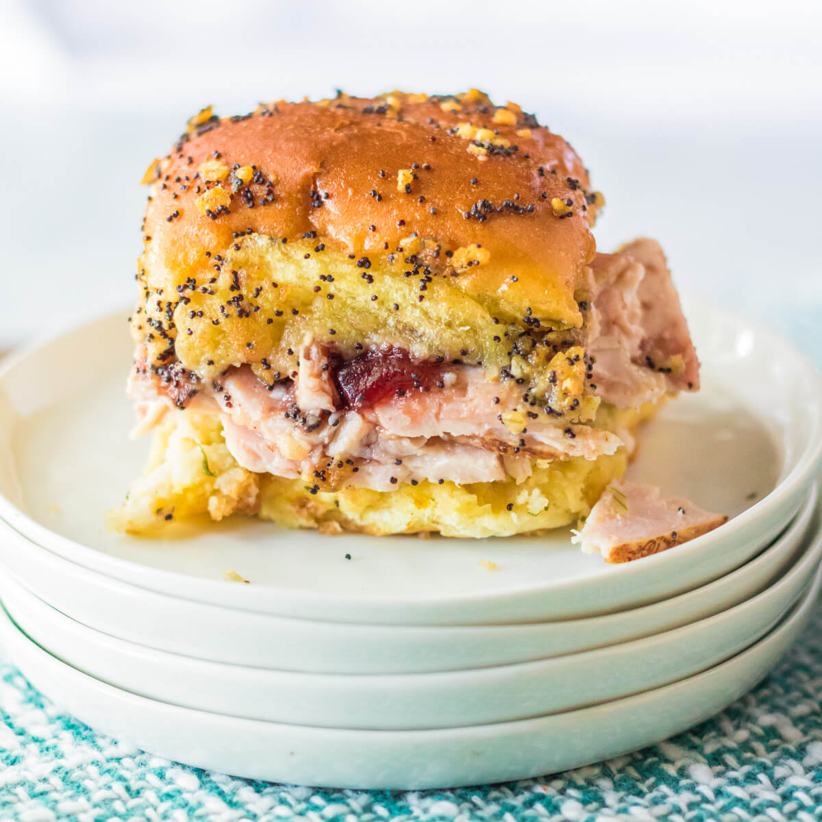 A golden baked Turkey Dinner slider in a Hawaiian Roll on a stack of white plates.