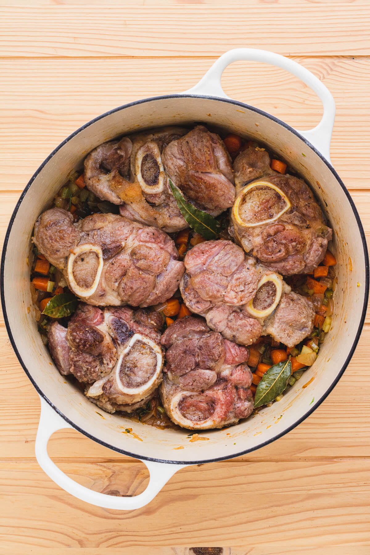 Browned osso bucco sit on top of aromatics and cooked soffritto in a large Dutch oven.