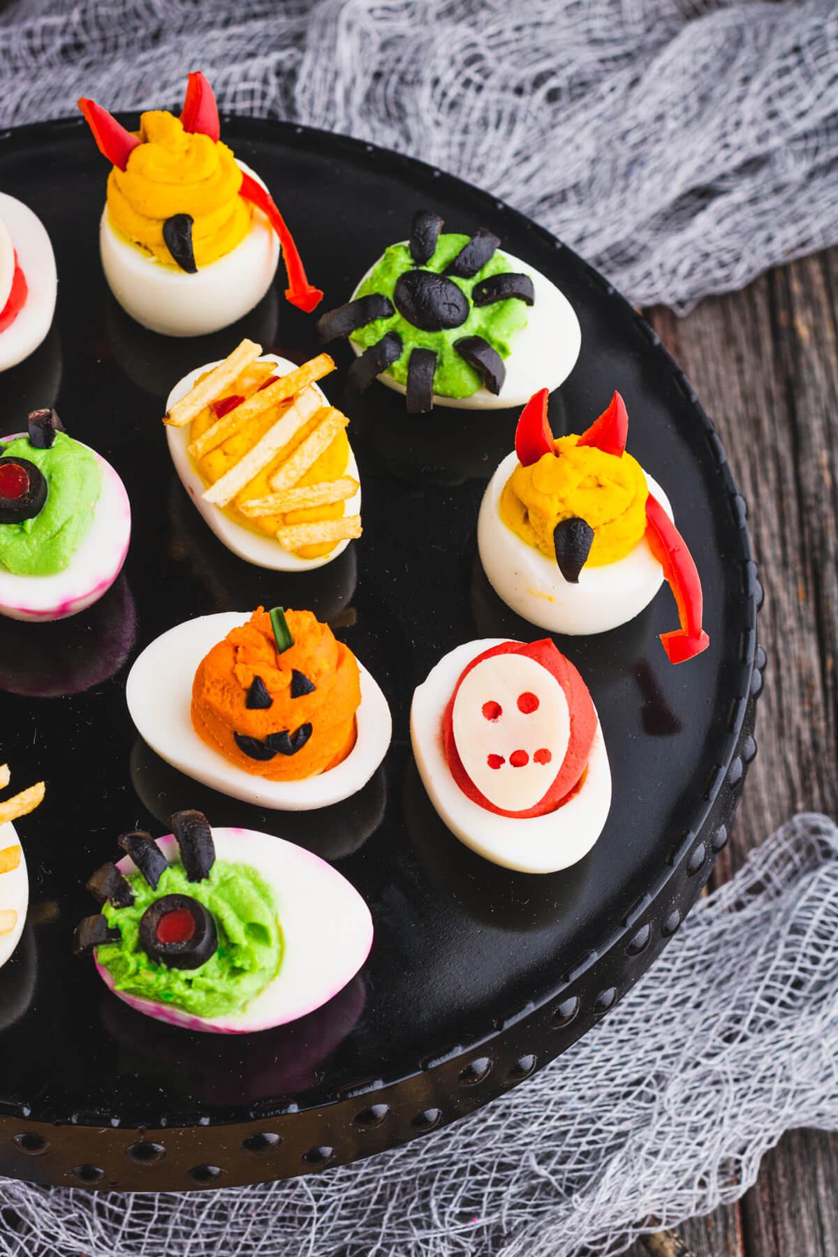 A black platter holds an assortment of creepy Halloween deviled eggs. 