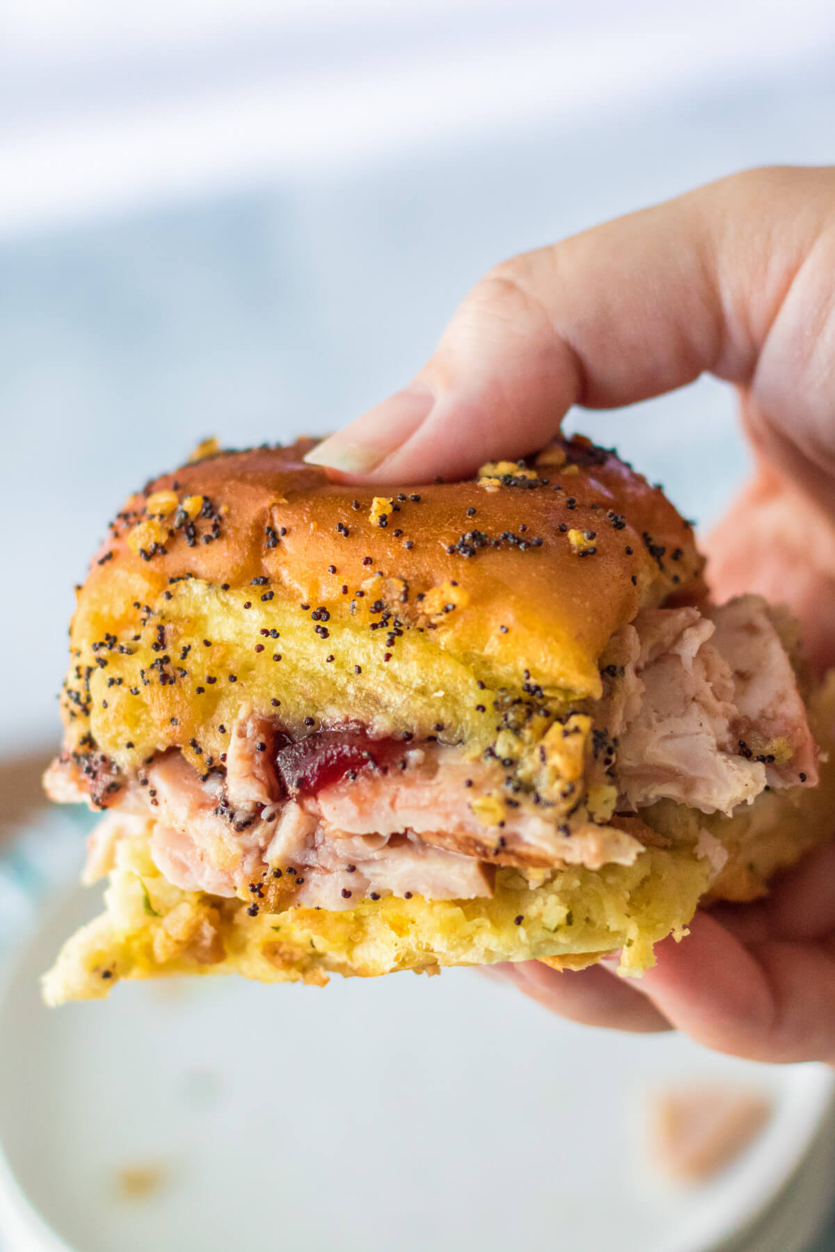 A hand holds one Hawaiian Roll Turkey Slider in the air.