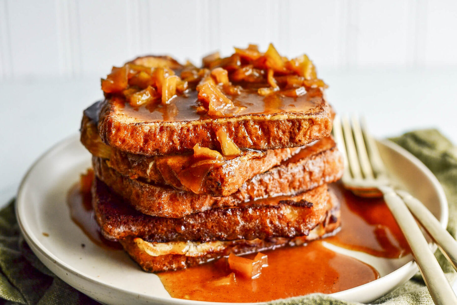 A stack of golden apple French toast topped with a rich caramel sauce on a white plate.