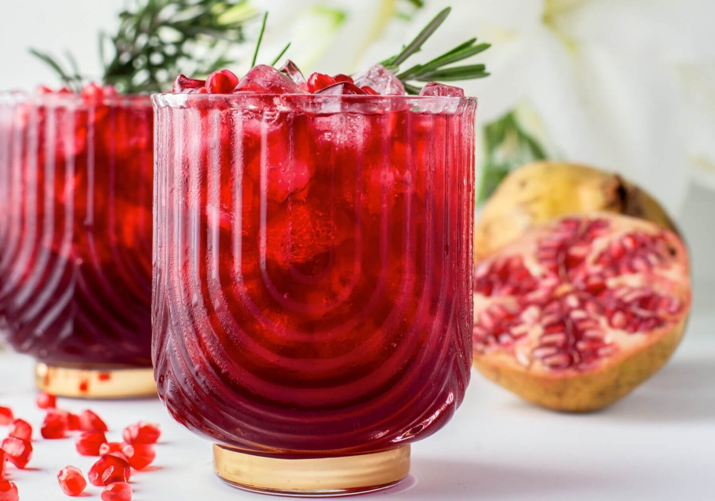 Two stunning ruby red cocktails in rocks glasses garnished with pomegranate arils and a sprig of rosemary.