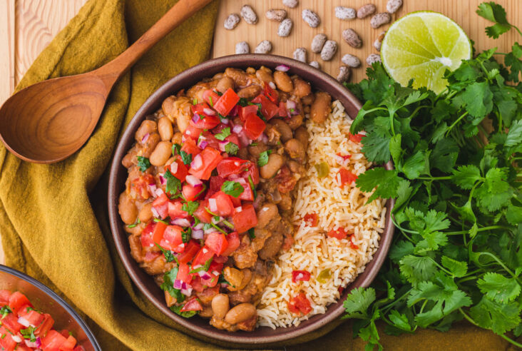 A bowl of creamy Pinto Beans and Rice surrounded by cilantro, lime, and dried pinto beans.