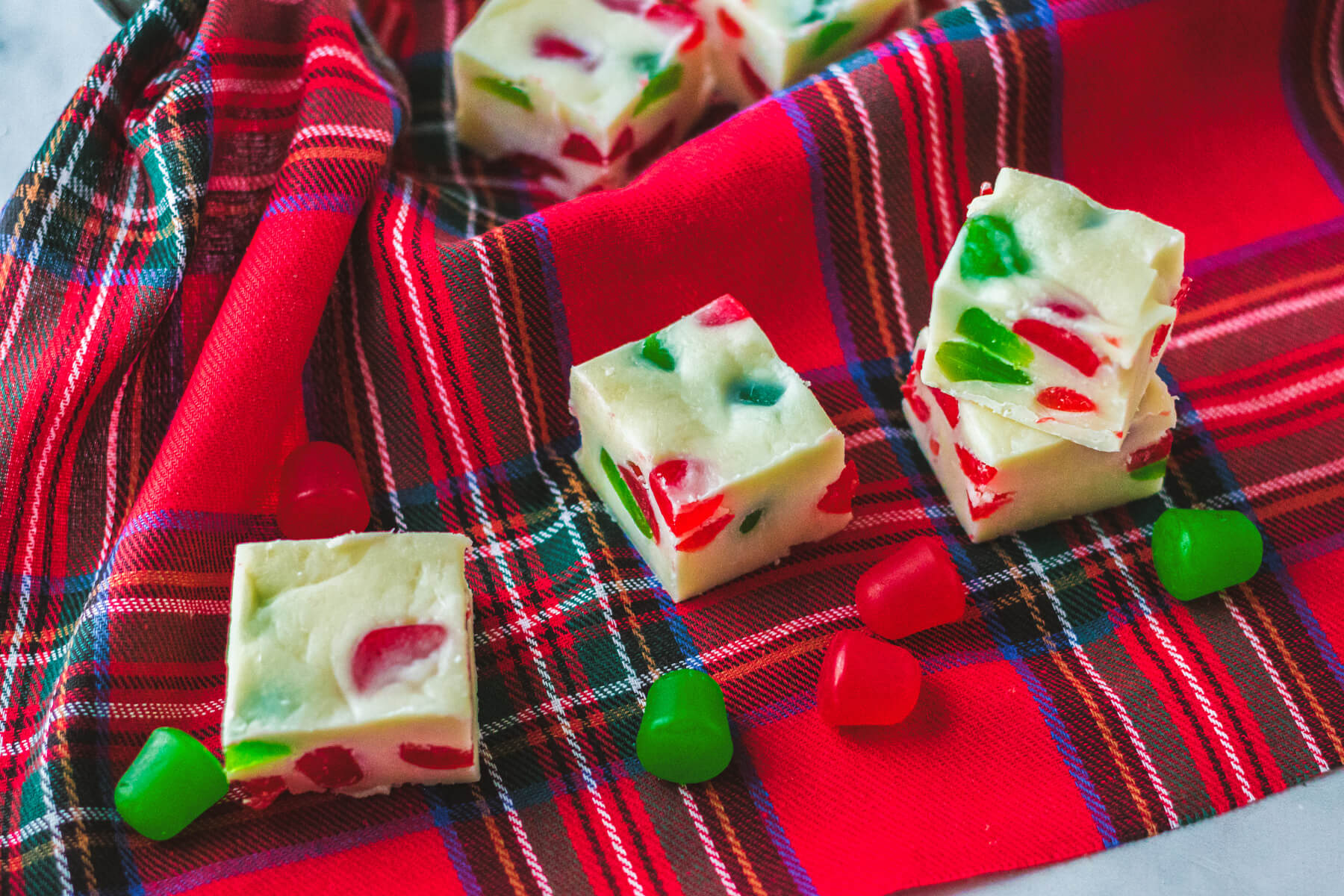 Three pieces of white fudge dotted with red and green gumdrop candies on a plaid napkin.
