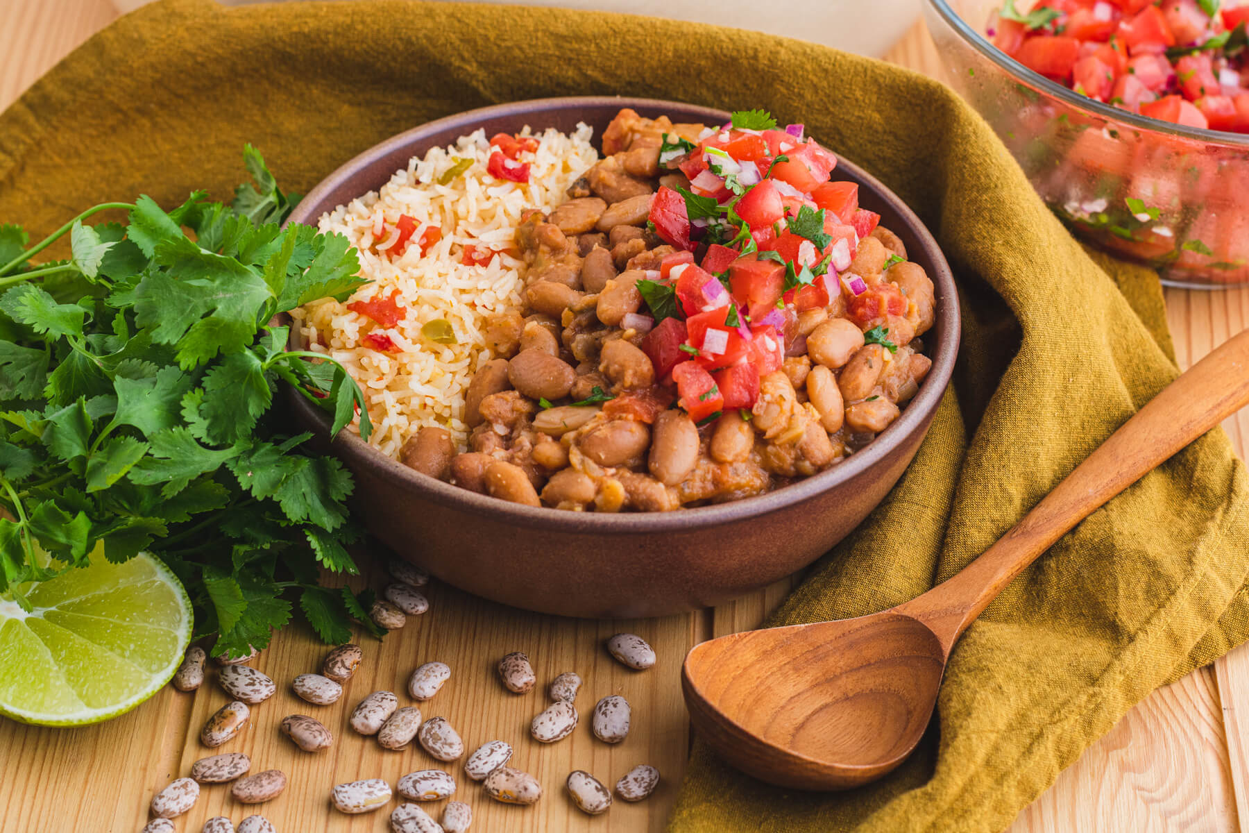 A bowl of creamy Pinto Beans and Rice surrounded by cilantro, lime, and dried pinto beans.