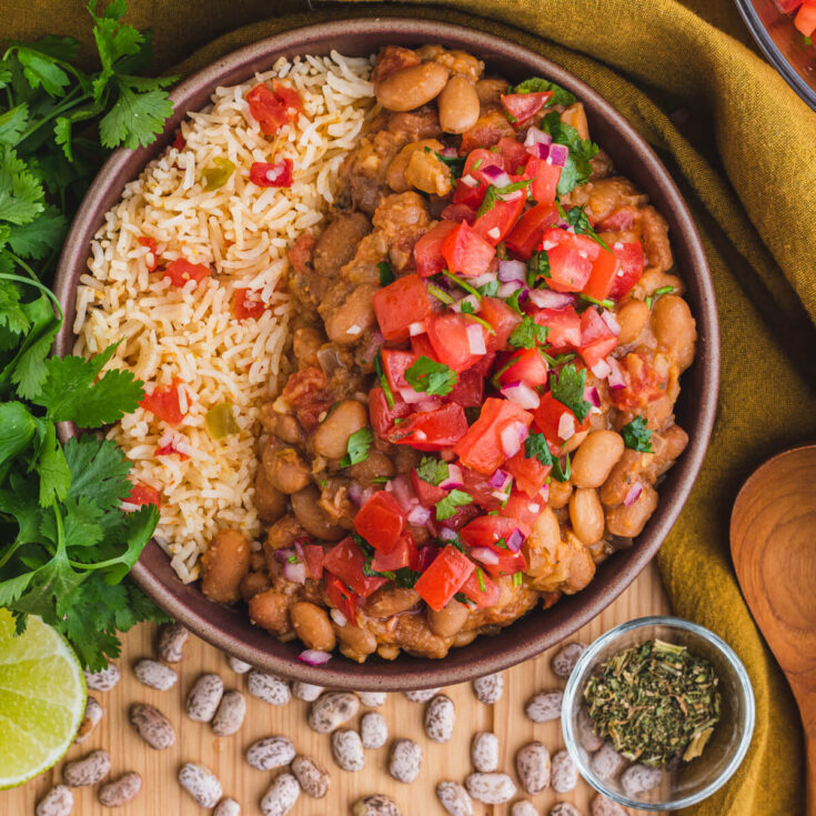 A bowl of creamy Pinto Beans and Rice surrounded by cilantro, lime, epazote, and dried pinto beans.