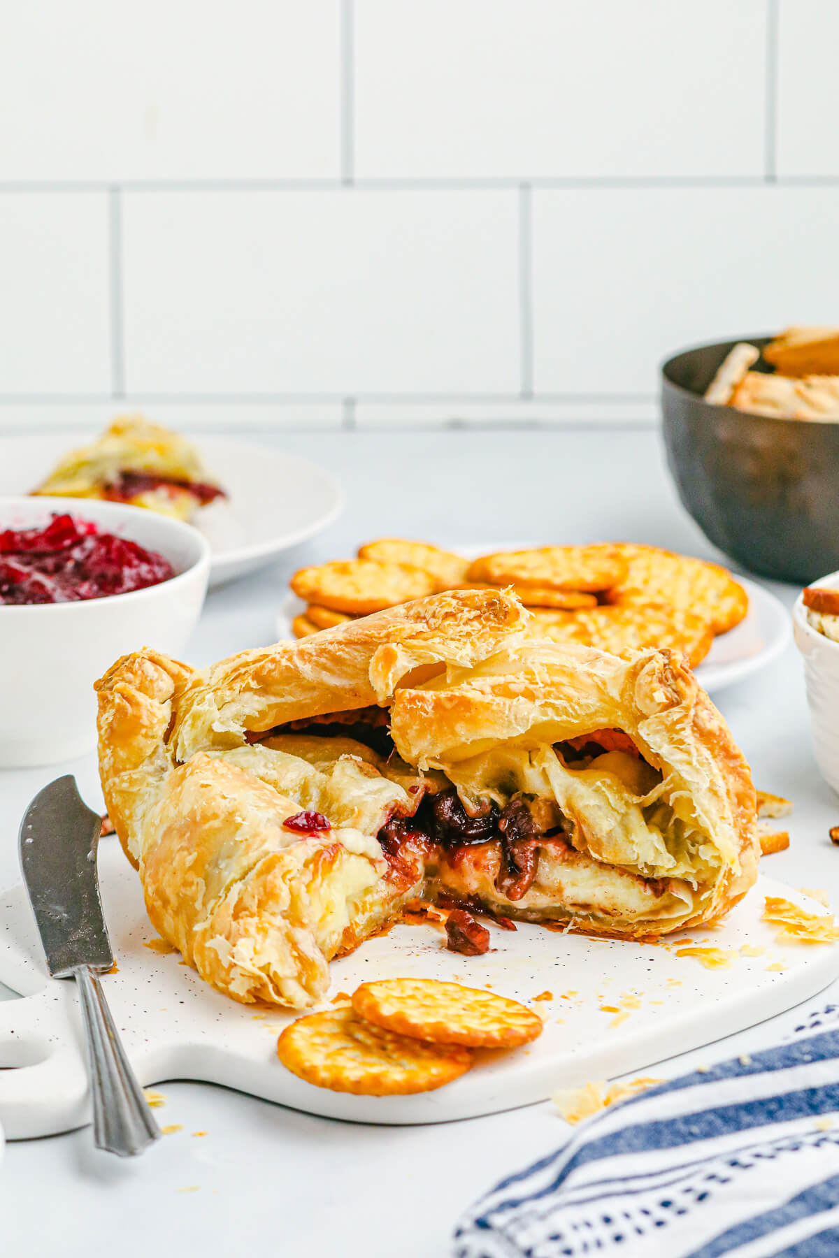 A golden Baked Brie en croute cut open to show the melted cheese, cranberries, and pecans inside.