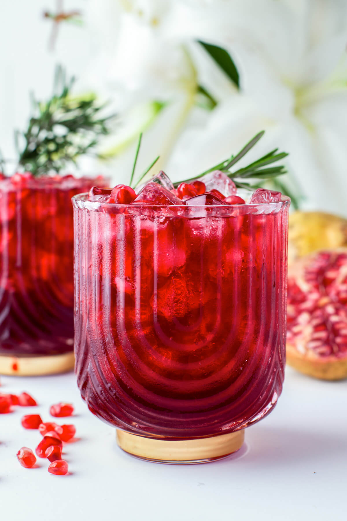 Two stunning rub red cocktails in rocks glasses garnished with pomegranate arils and a sprig of rosemary.
