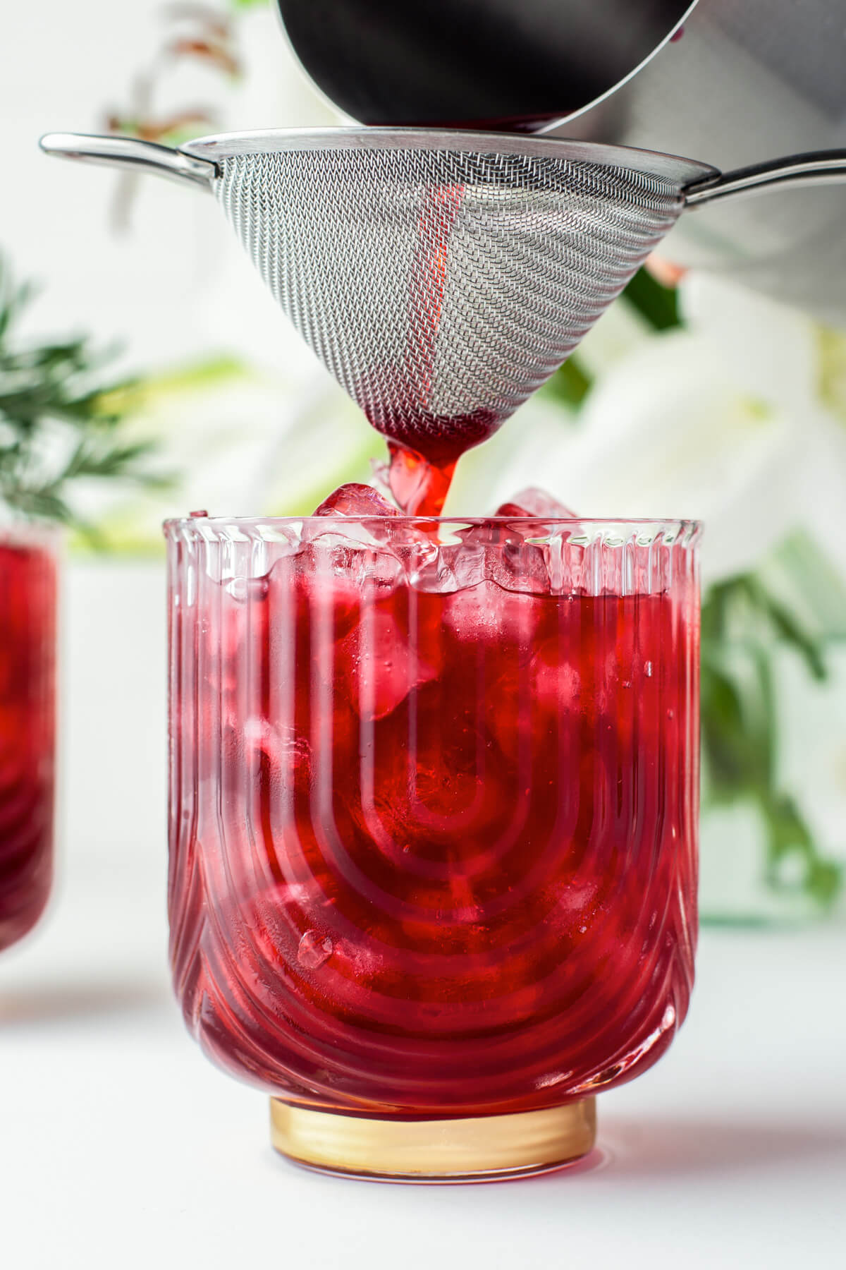 Straining the ruby red Hibiscus Pomegranate Margarita into an ice filled rocks glass.