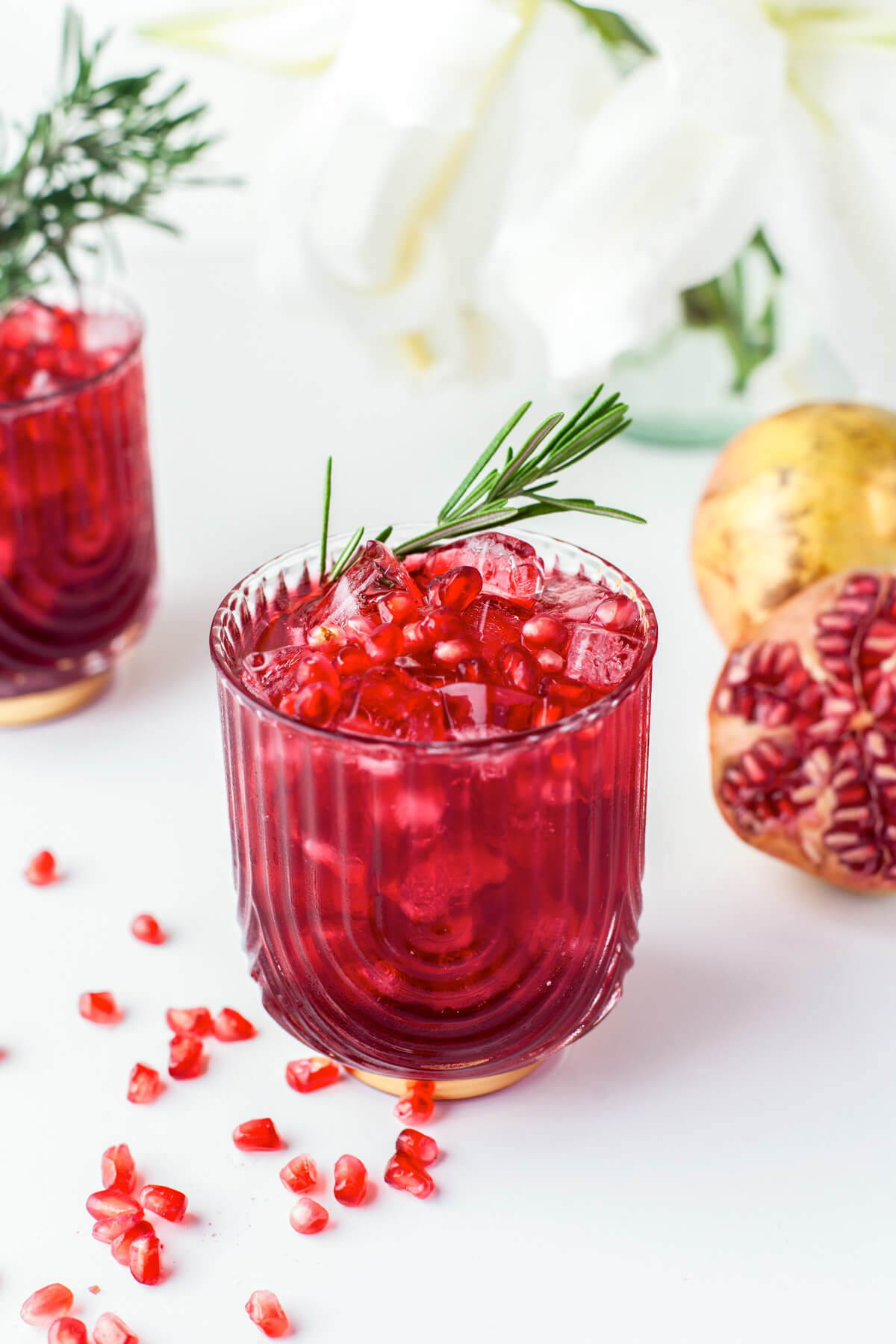 A stunning ruby red cocktail in a rocks glass garnished with pomegranate arils and a sprig of rosemary.