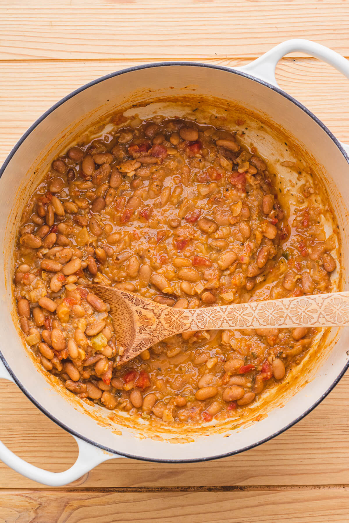 Cooked pinto beans swirled with a wooden spoon in a Dutch oven.