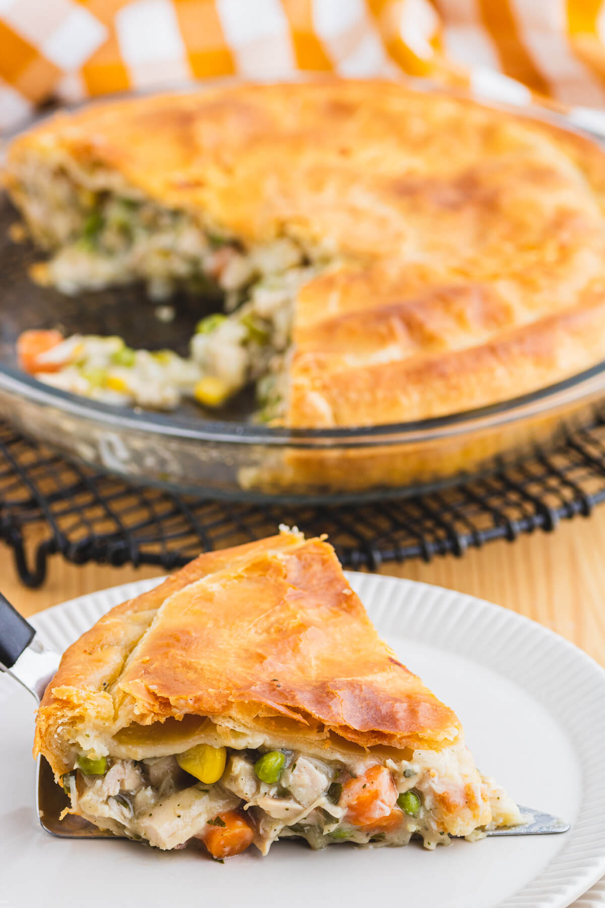 A golden flaky turkey pot pie with a slice missing and on a plate in front of the pie.