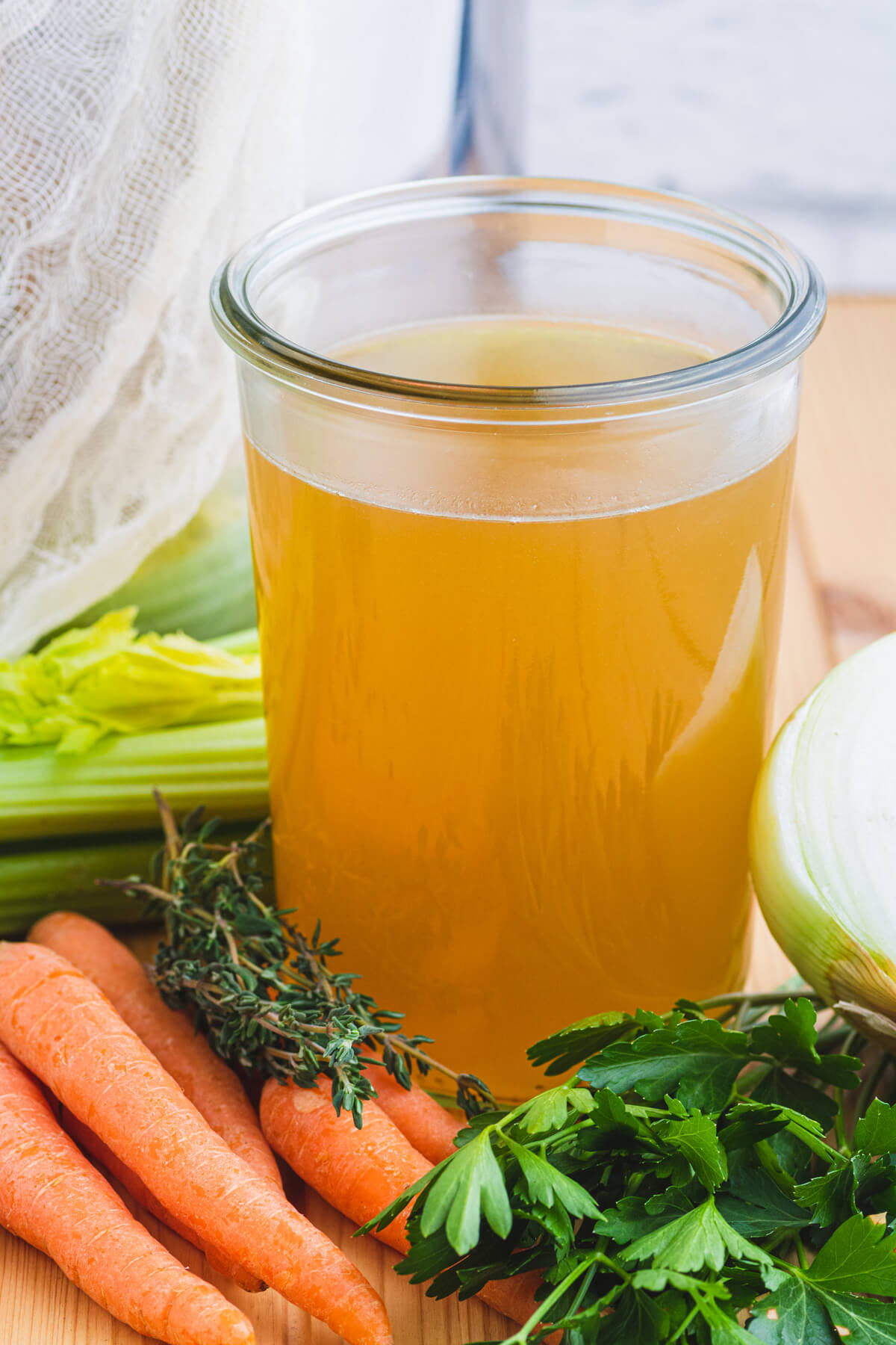 A glass quart jar filled with rich yellow turkey stock beside fresh vegetables and a large stock pot.