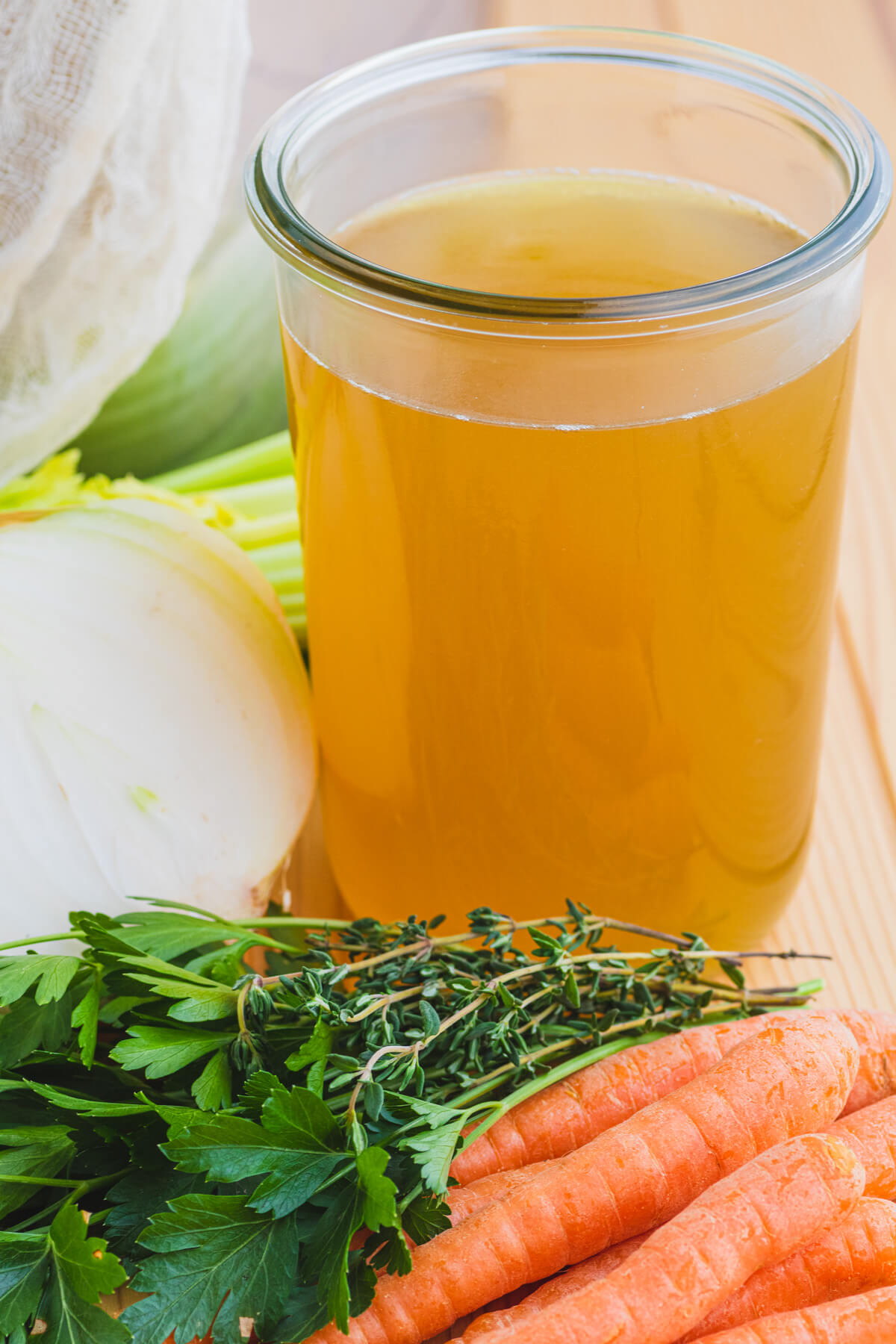 A glass quart jar filled with rich yellow turkey stock beside fresh vegetables and a large stock pot.