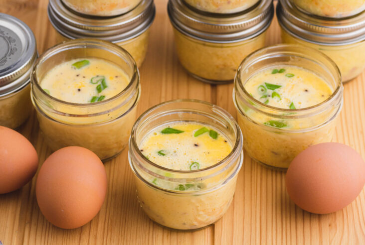 Three sous vide egg bites in glass jars surrounded by brown eggs.