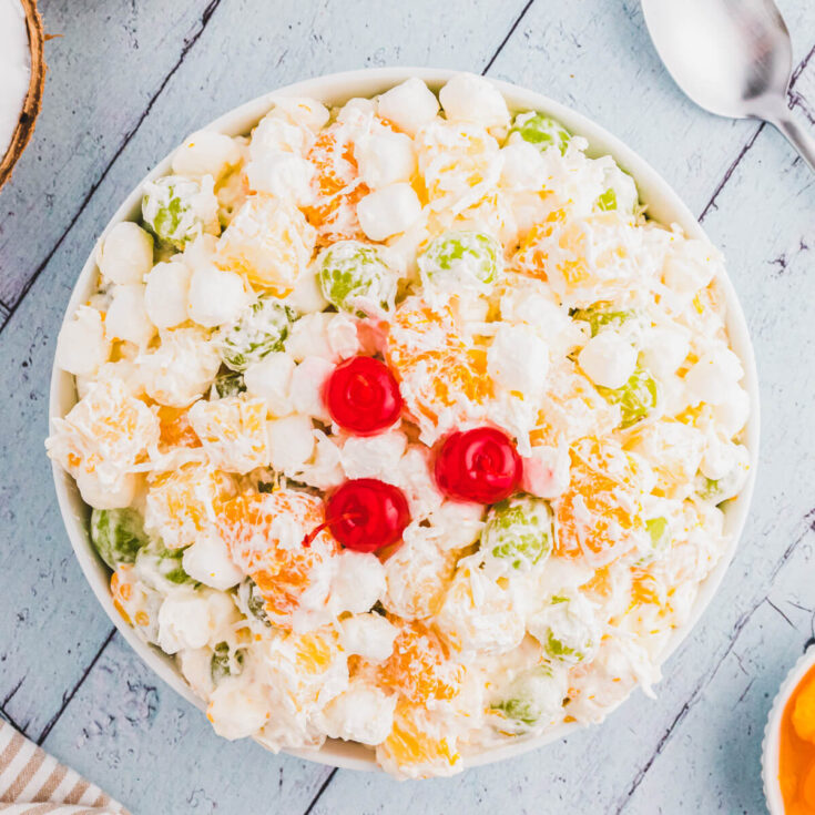 A white bowl of fluffy dreamy Ambrosia fruit salad on a light blue background.