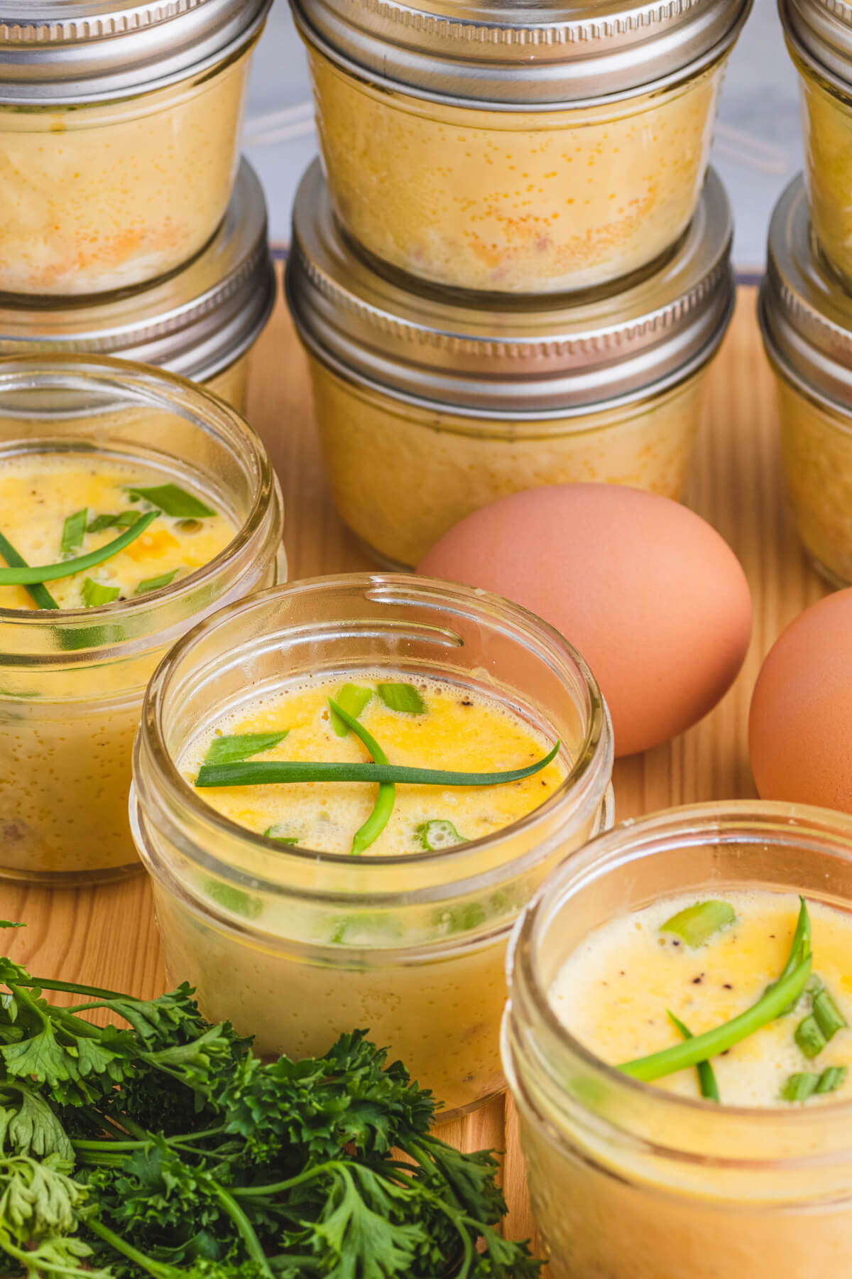 Three sous vide egg bites in glass jars surrounded by fresh parsley and brown eggs.