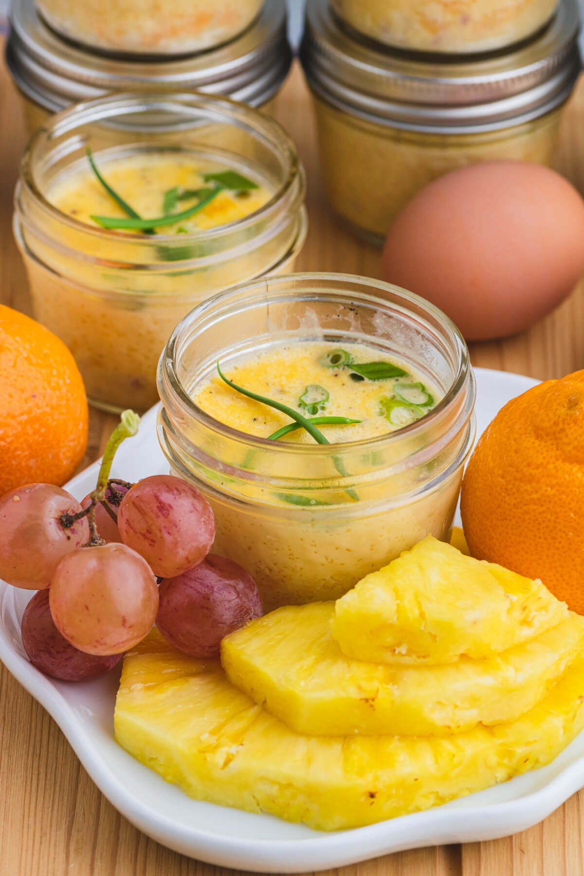 Two sous vide egg bites in glass jars on a white plate surrounded by fresh fruit..