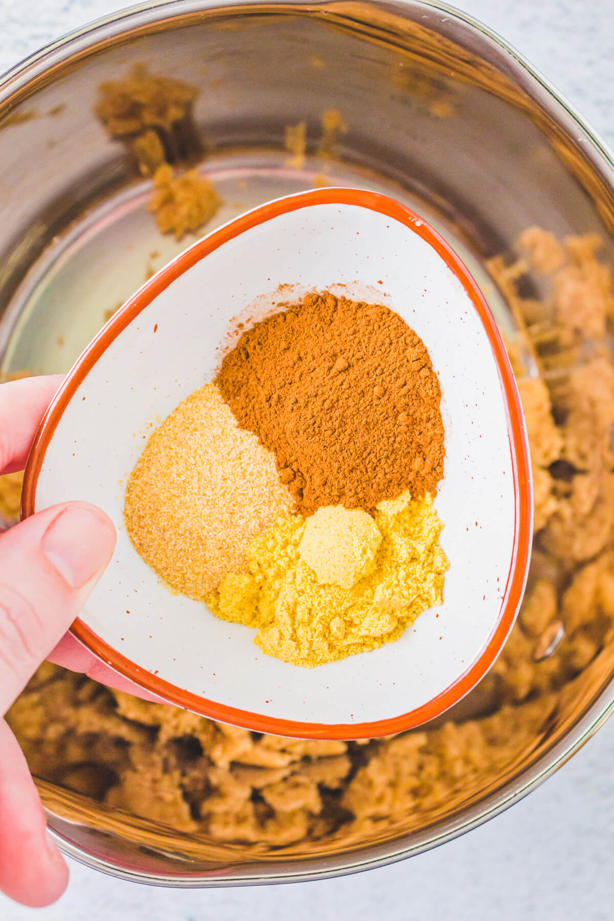 Ground mustard and spices in a small bowl held over a larger bowl of brown sugar.