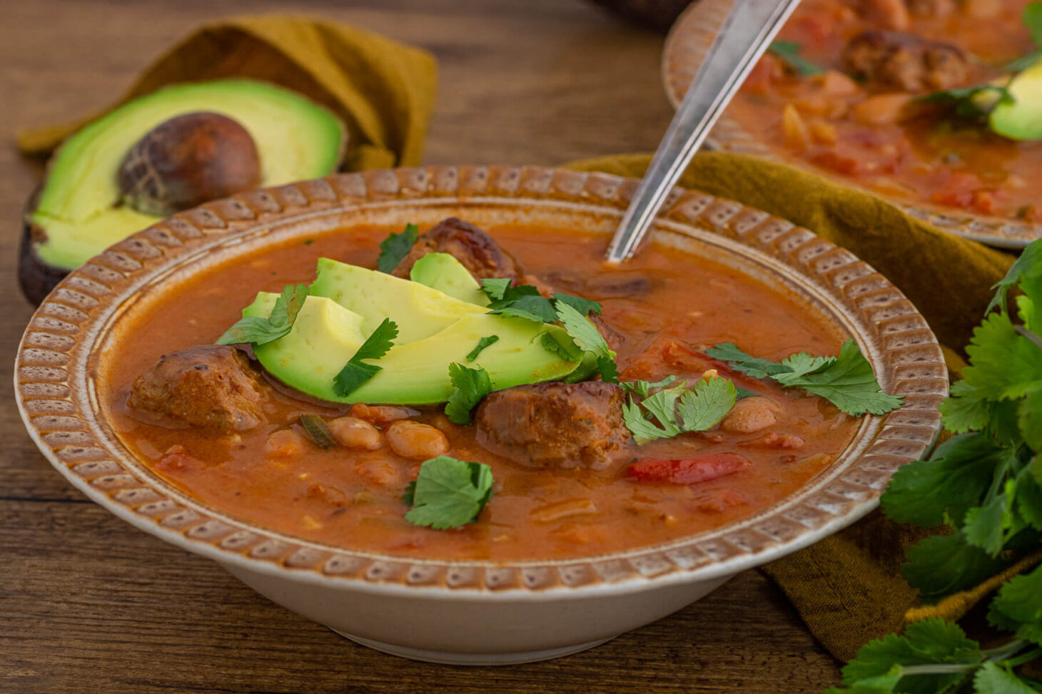 An inviting bowl of spicy Pinto Bean Soup garnished with sliced avocado and fresh cilantro.