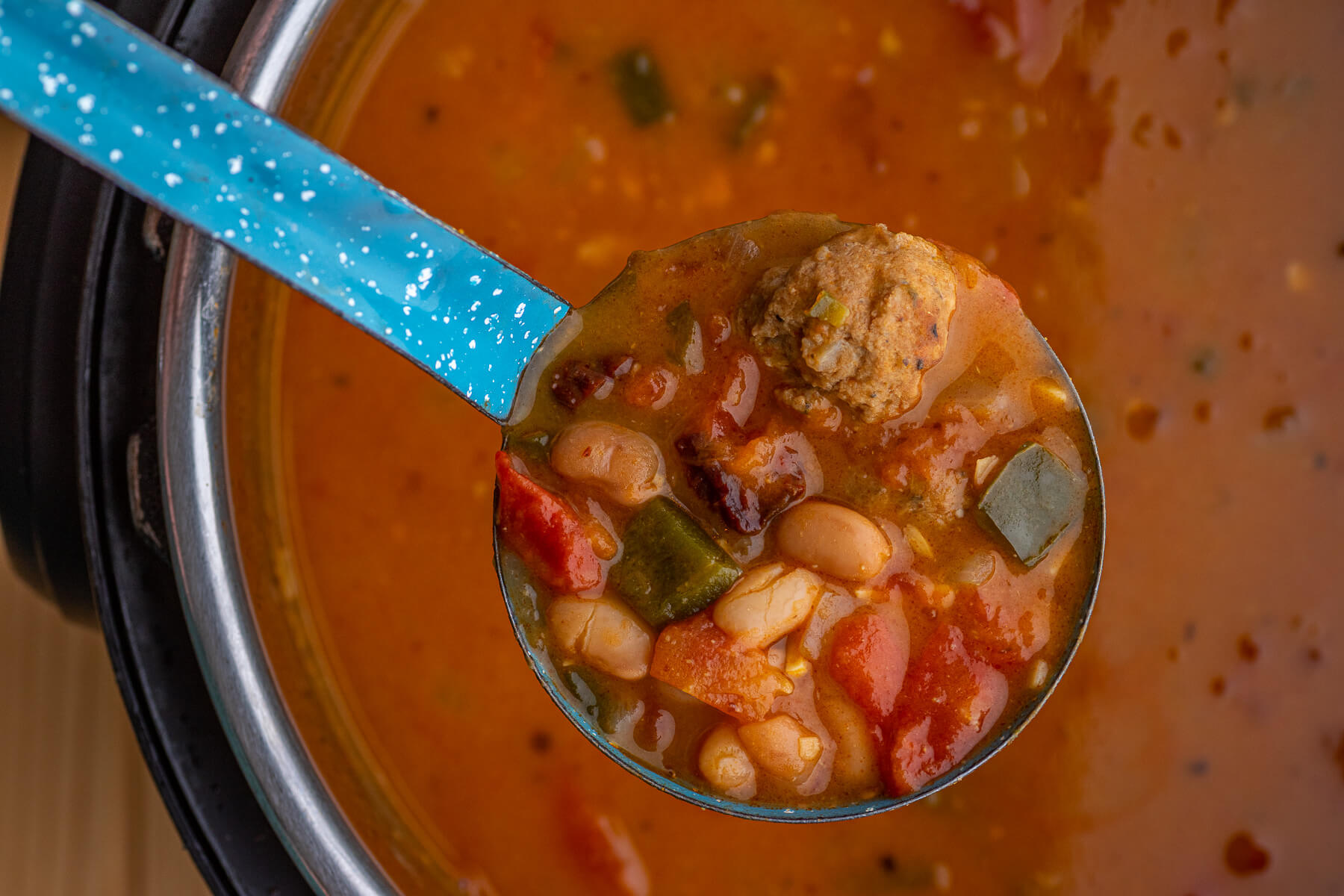 A blue enamel ladle filled with a serving of spicy Pinto Bean Soup.