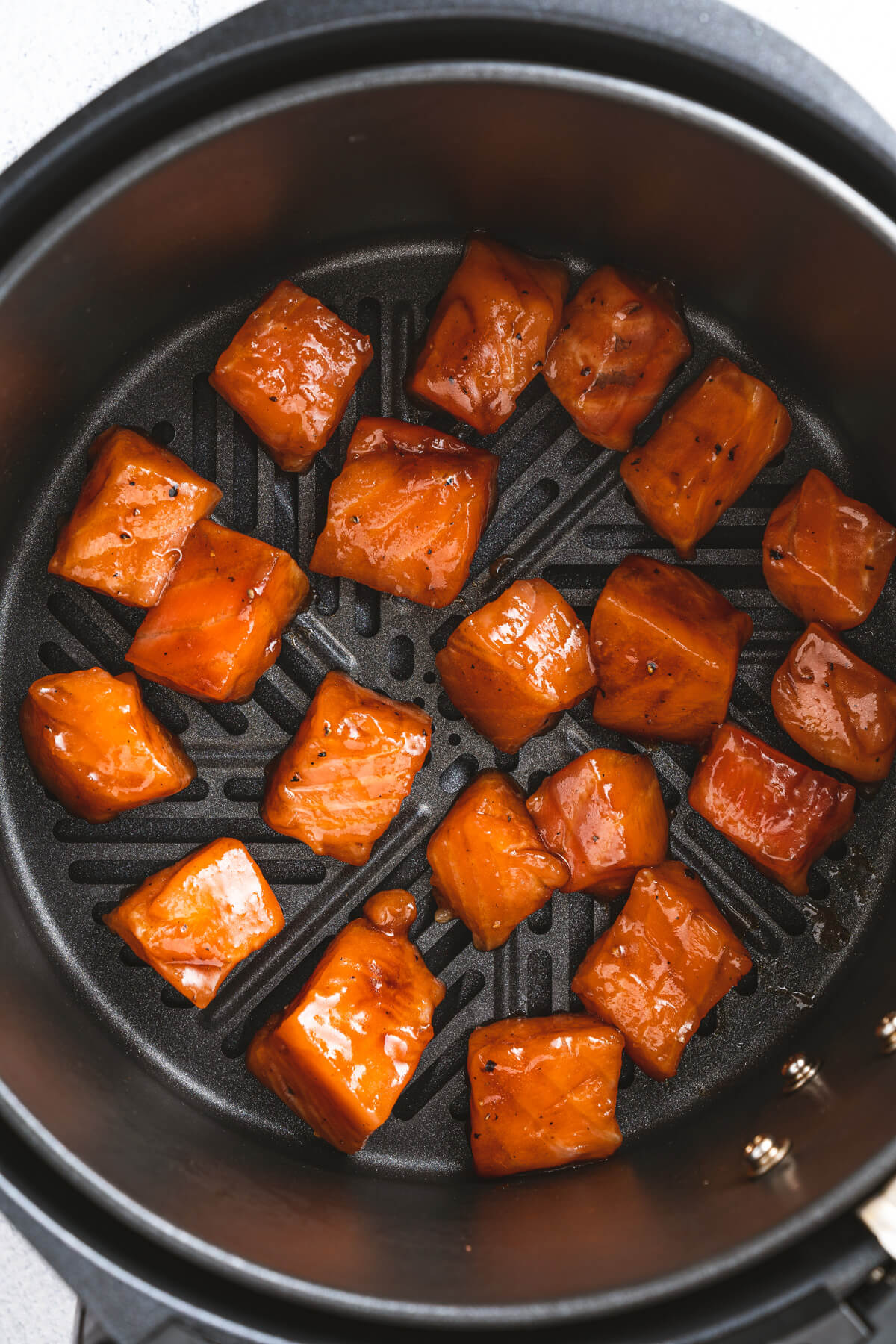 Teriyaki glazed raw salmon cubes in an air fryer basket.