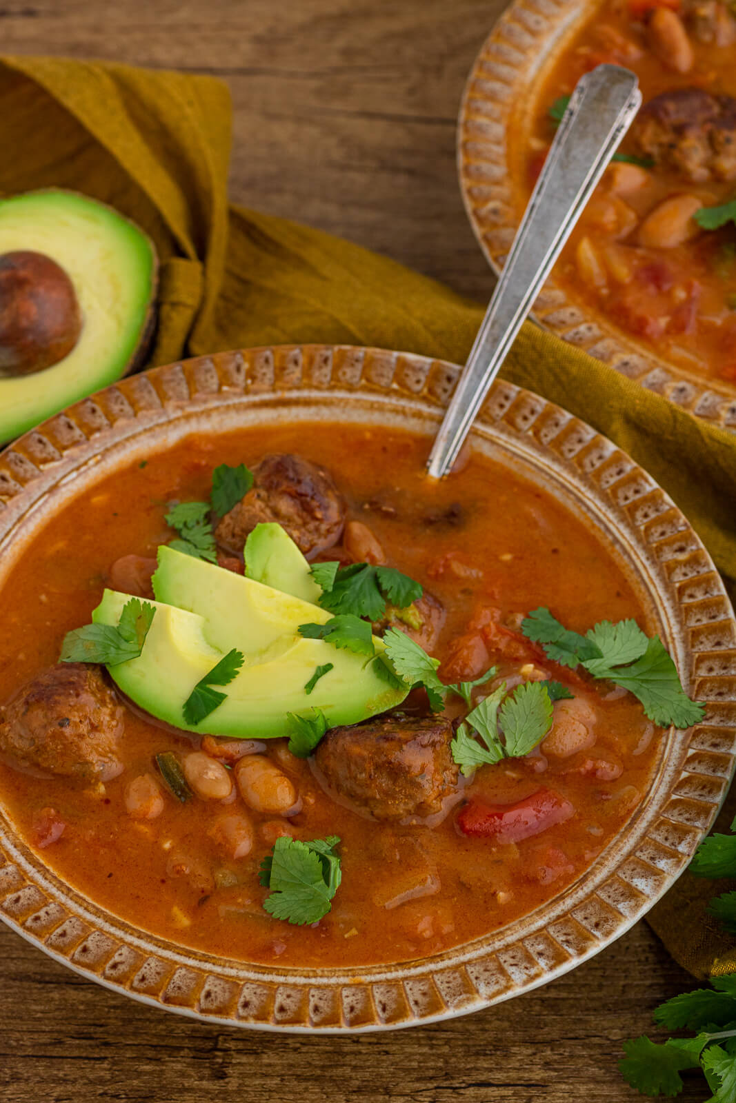 An inviting bowl of spicy Pinto Bean Soup garnished with sliced avocado and fresh cilantro.