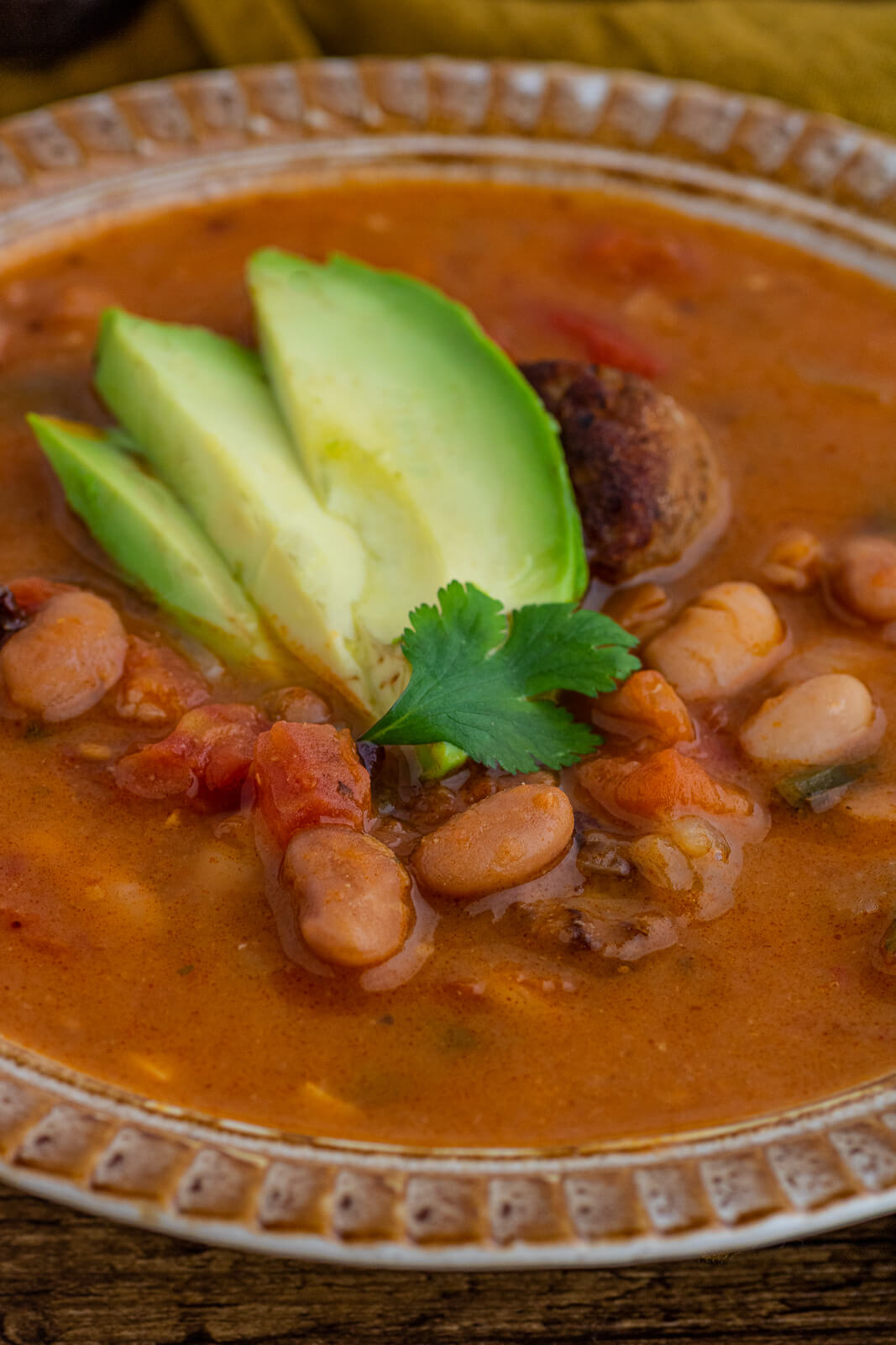 Close up of spicy Pinto Bean Soup garnished with sliced avocado.