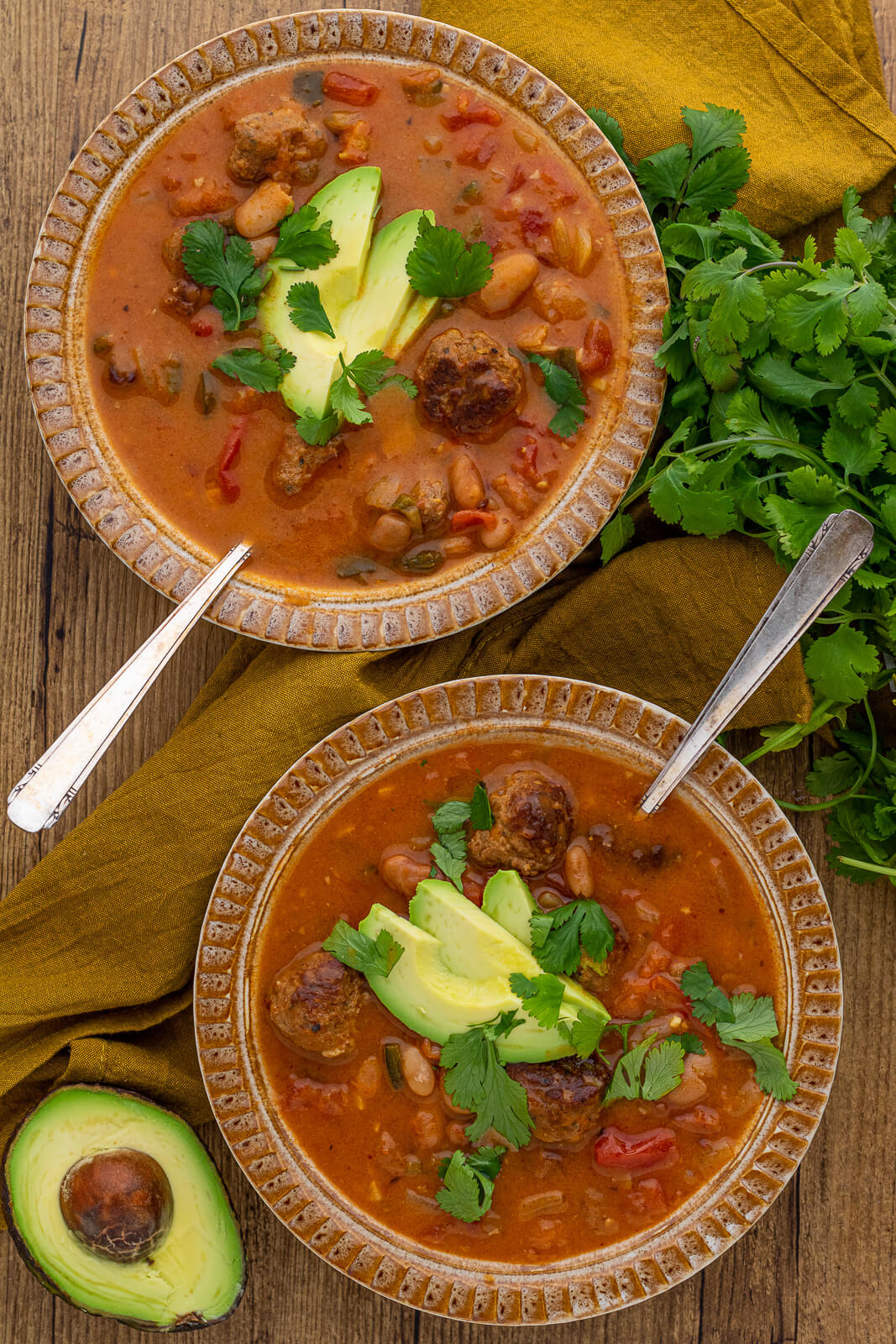 Two inviting bowls of spicy Pinto Bean Soup garnished with sliced avocado and fresh cilantro.