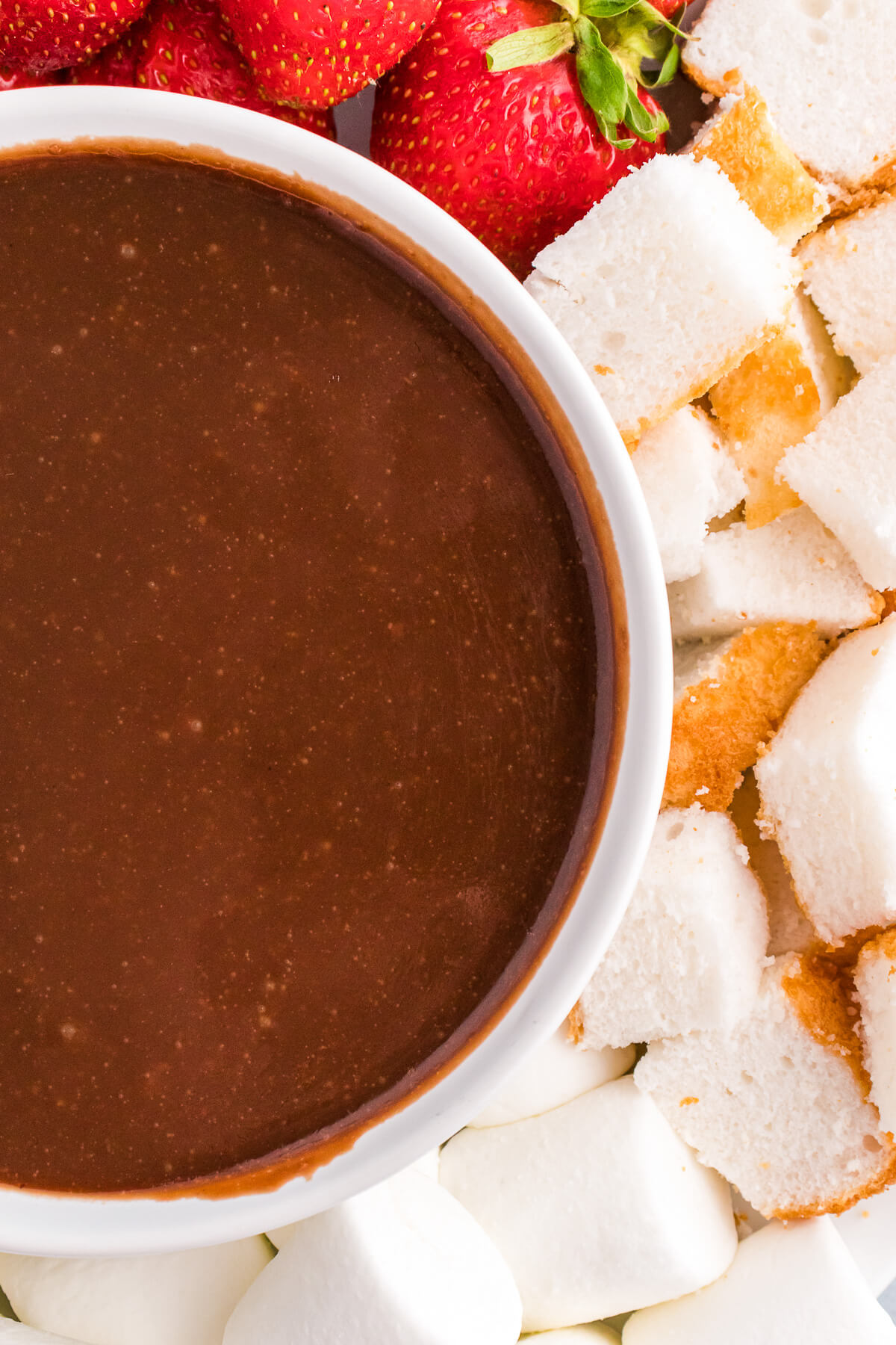 A dessert platter featuring a bowl of melted chocolate fondue surrounded by items for dipping.