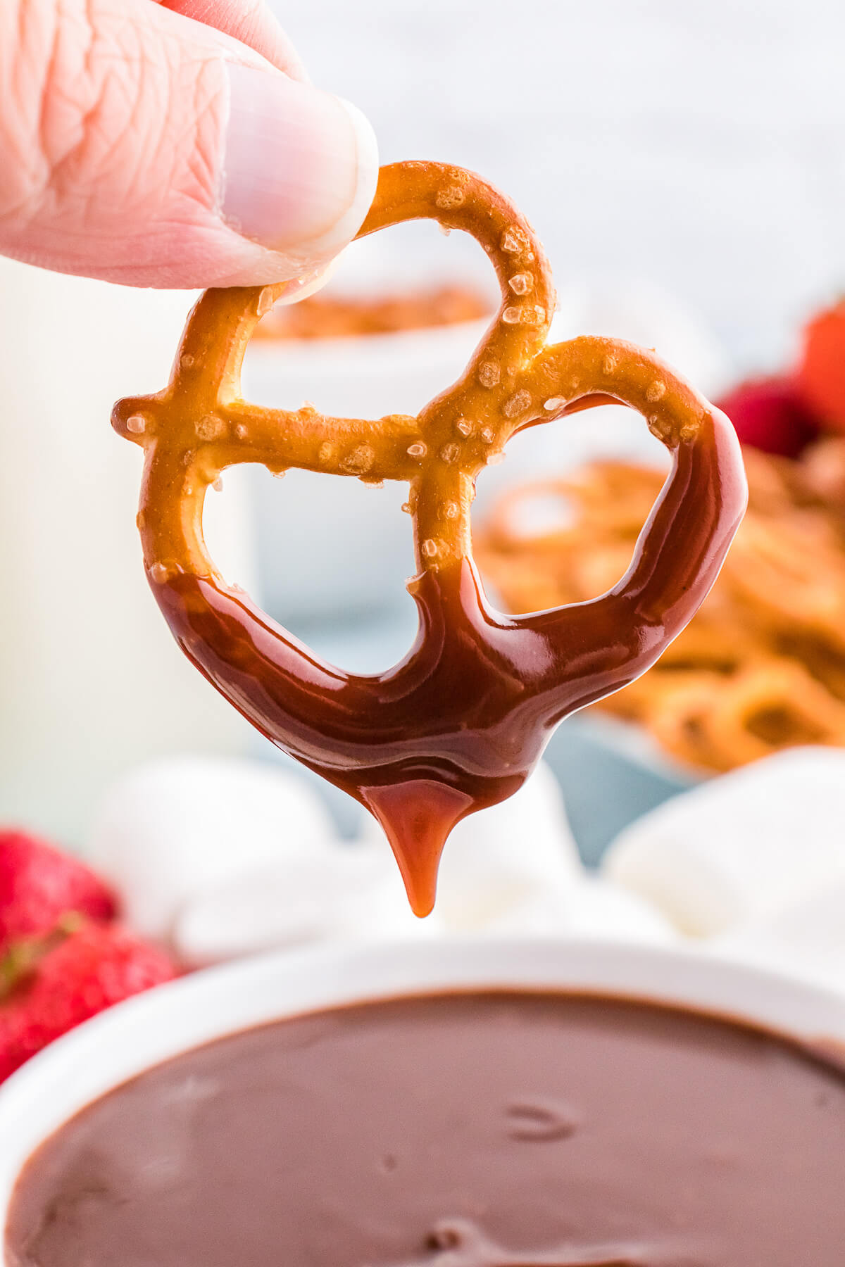 A hand holds a pretzel dripping over a chocolate fondue. 