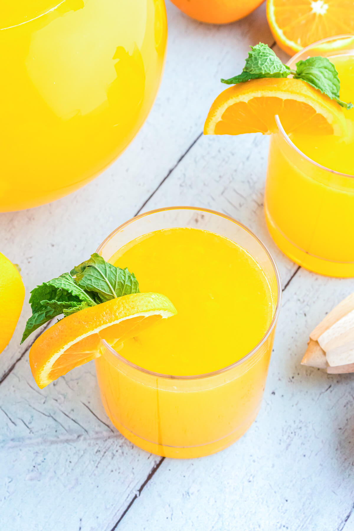 Two glasses of bright homemade orangeade garnished with orange wheels and green sprigs of fresh mint.