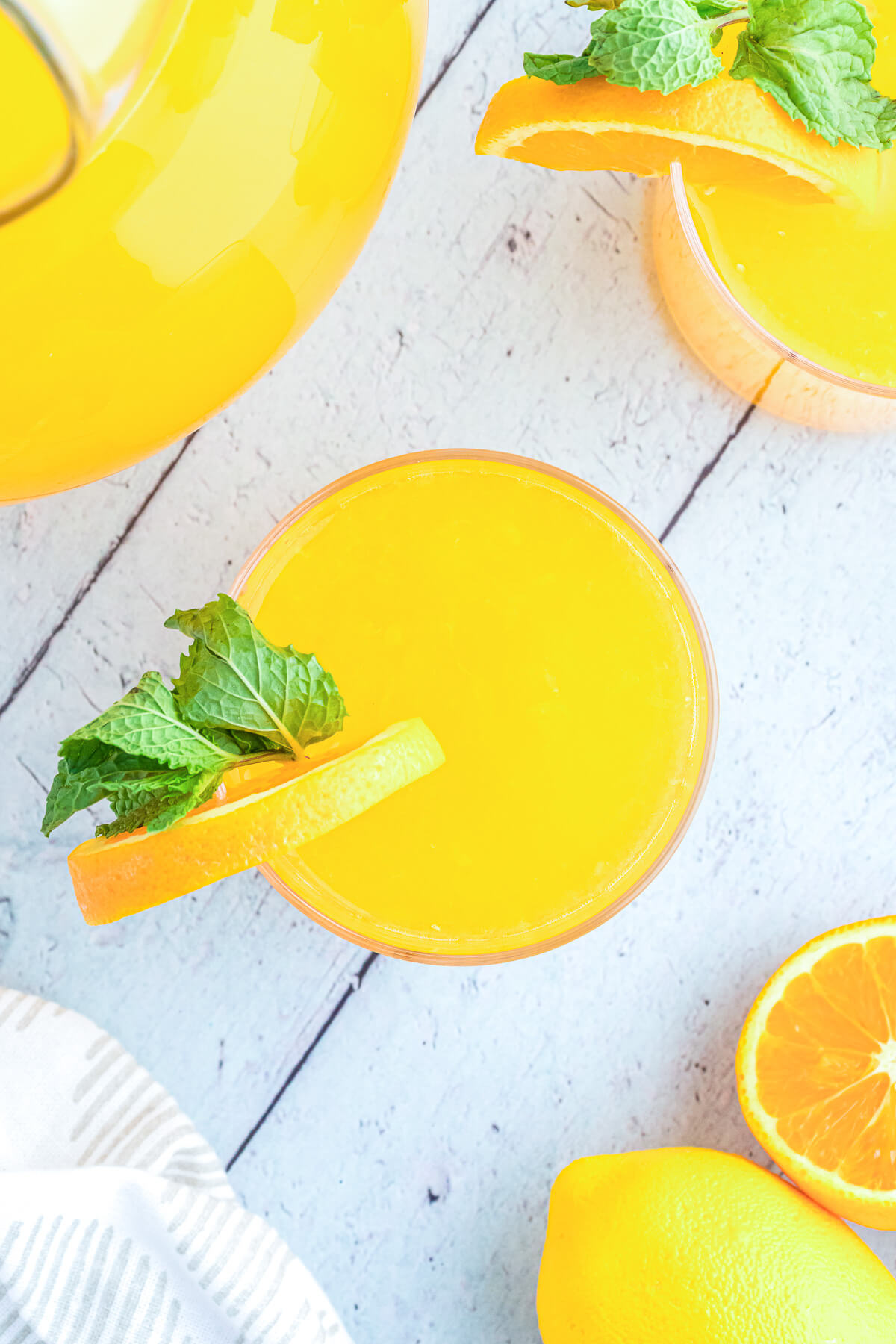 A glass of bright homemade orangeade garnished with orange wheels and green sprigs of fresh mint.