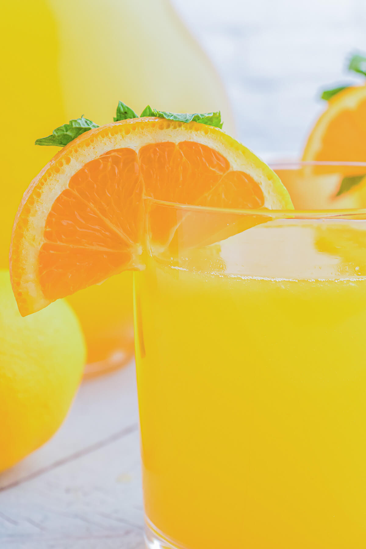 A glass of bright homemade orangeade garnished with orange wheels and green sprigs of fresh mint.
