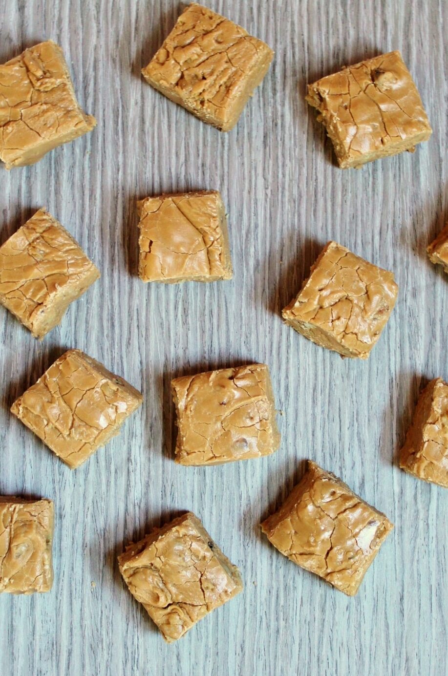 Cut squares of light brown maple fudge on a grey wooden background.