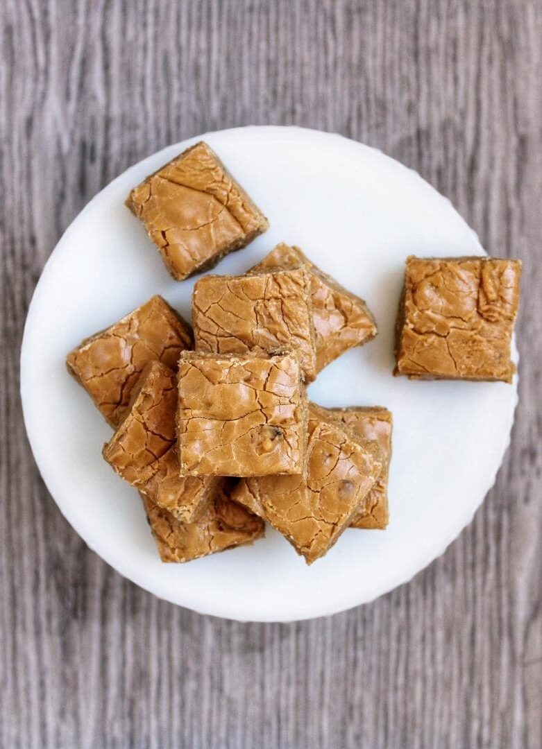 A white plate of light brown maple fudge on a grey wooden table.