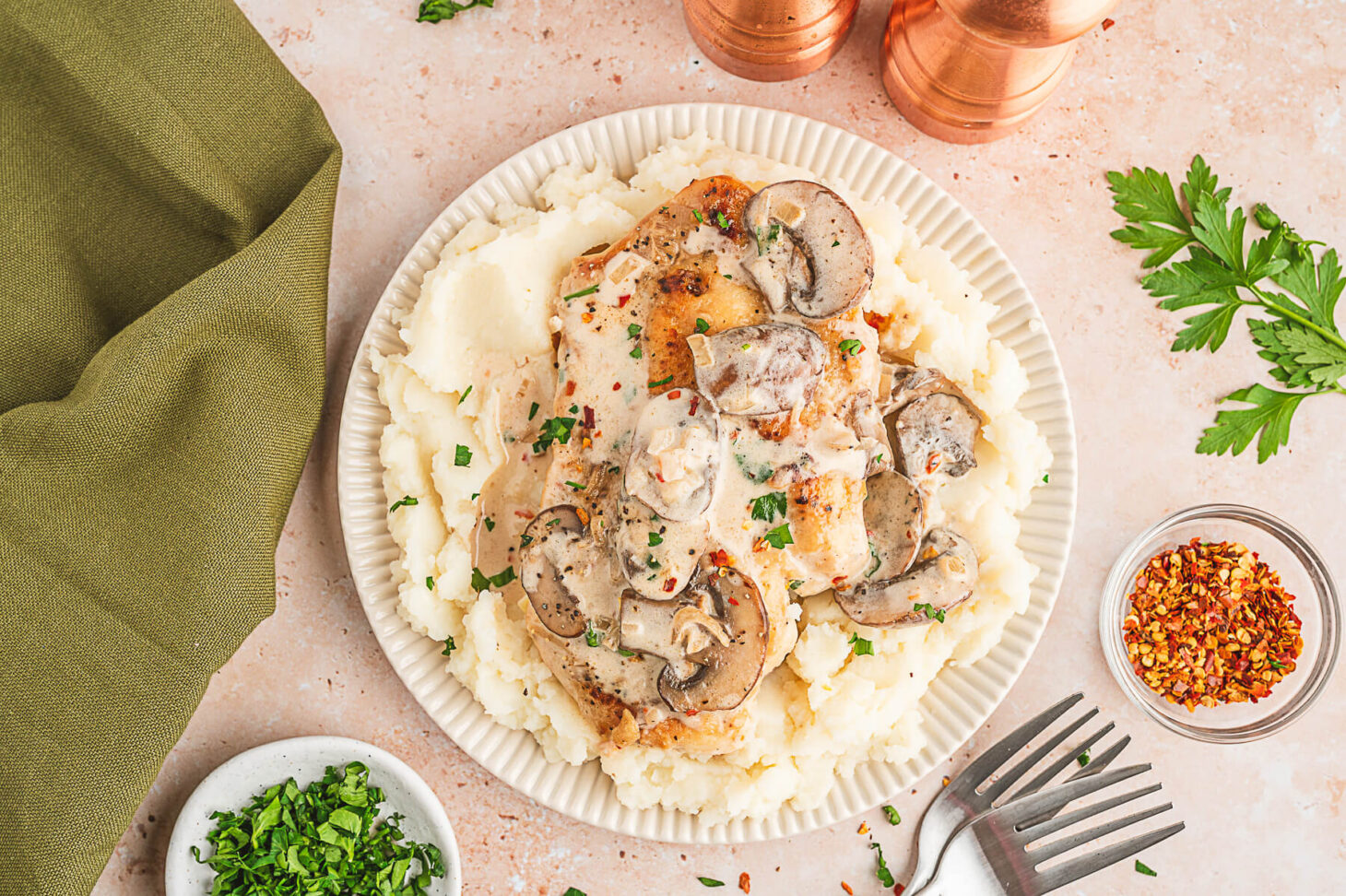 A serving of creamy chicken marsala featuring a whole chicken breast topped with mushrooms and creamy sauce over a bed of mashed potatoes.
