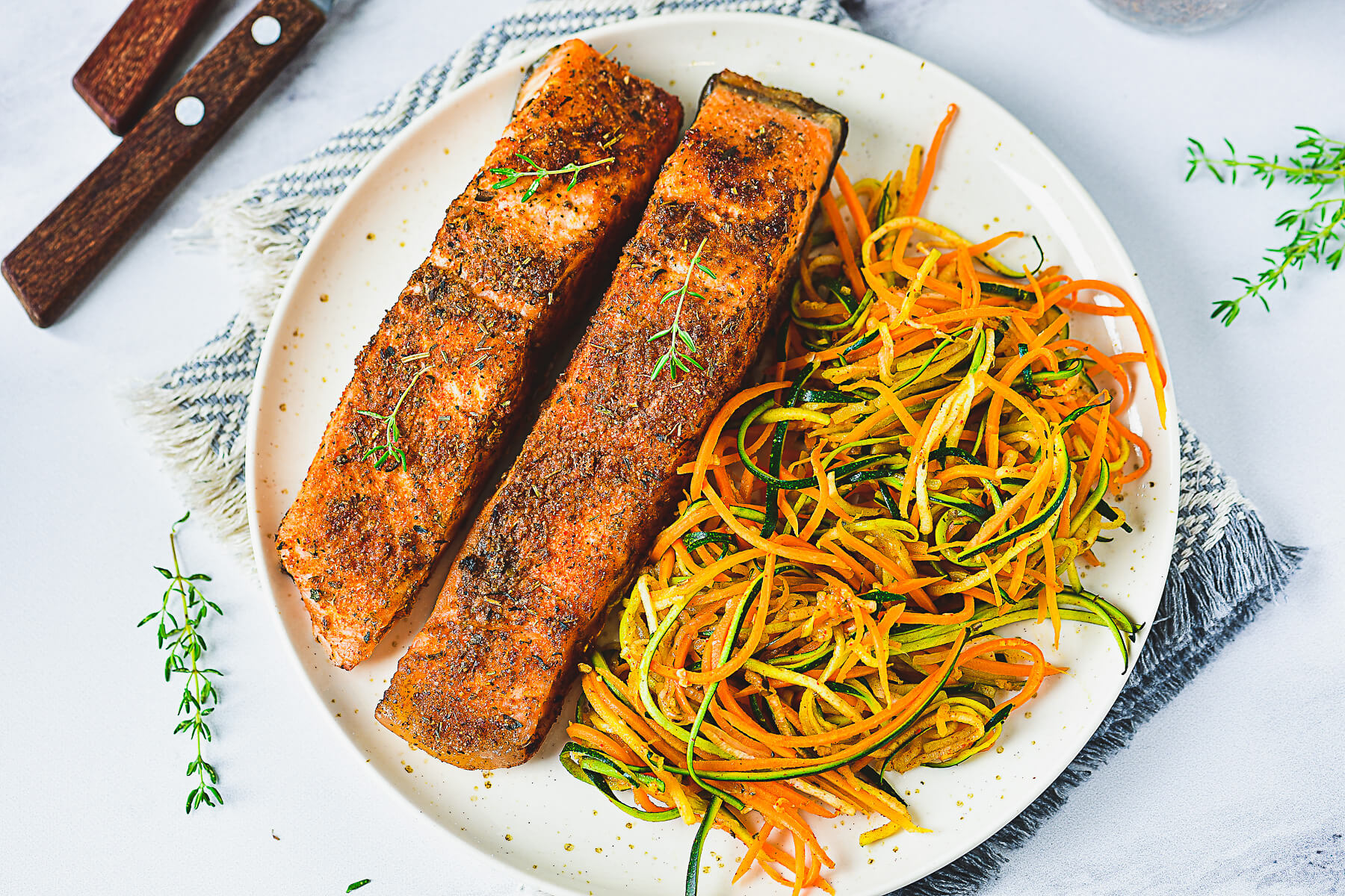 Two cooked spiced salmon fillets on a plate beside spiralized vegetables.