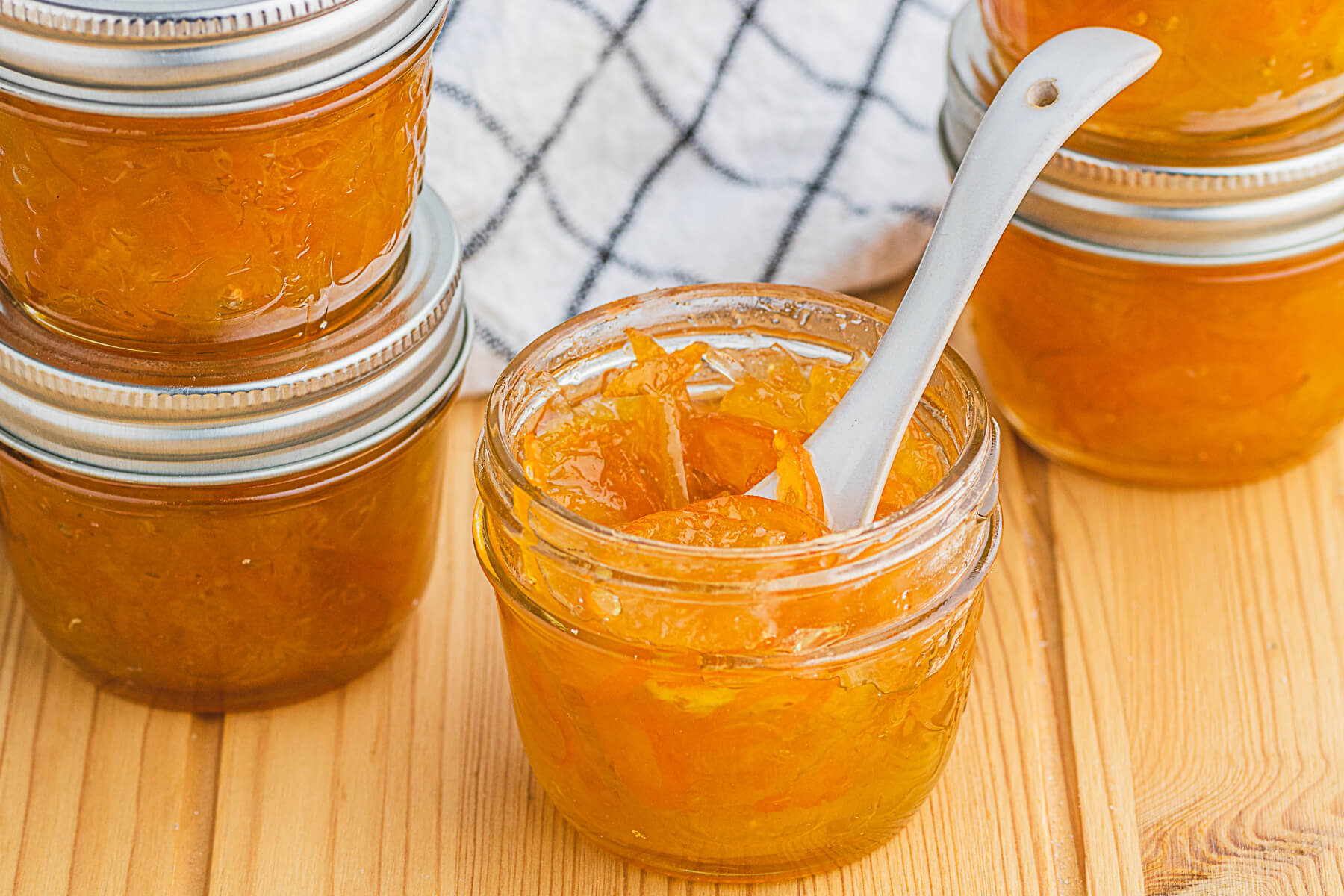 Four jars of Kumquat Marmalade surround an open marmalade jar with a spoon inside.