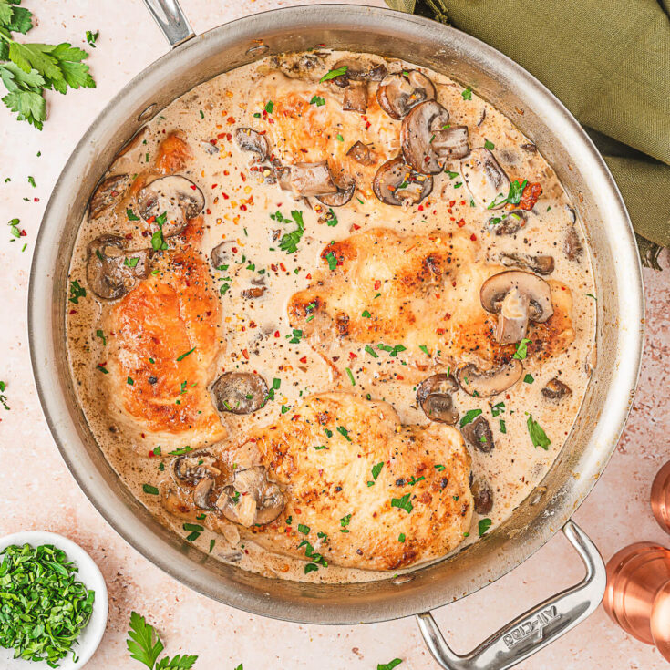 Cooked chicken breasts and mushrooms swimming in a saucepan of creamy marsala sauce.