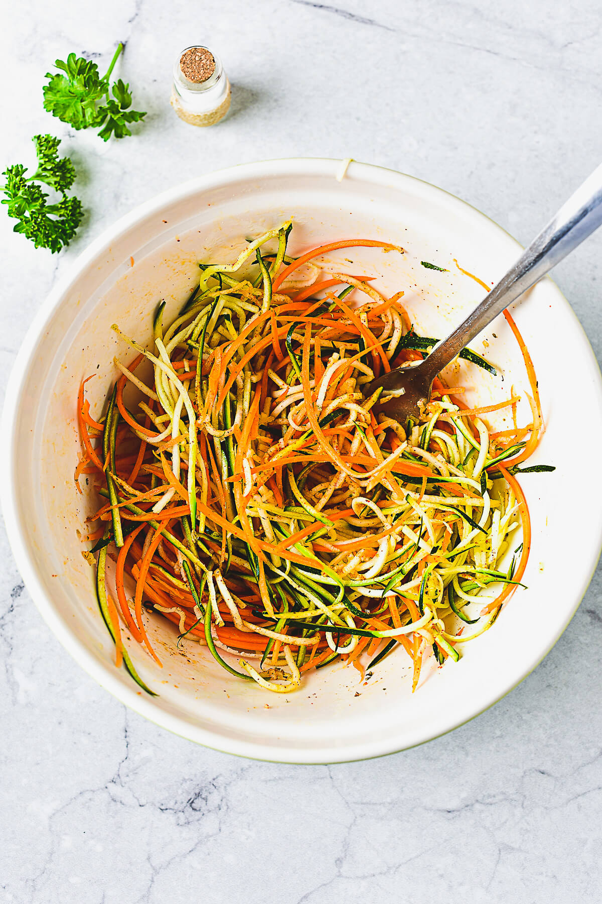 A white bowl full of seasoned spiralized zucchini and carrots.