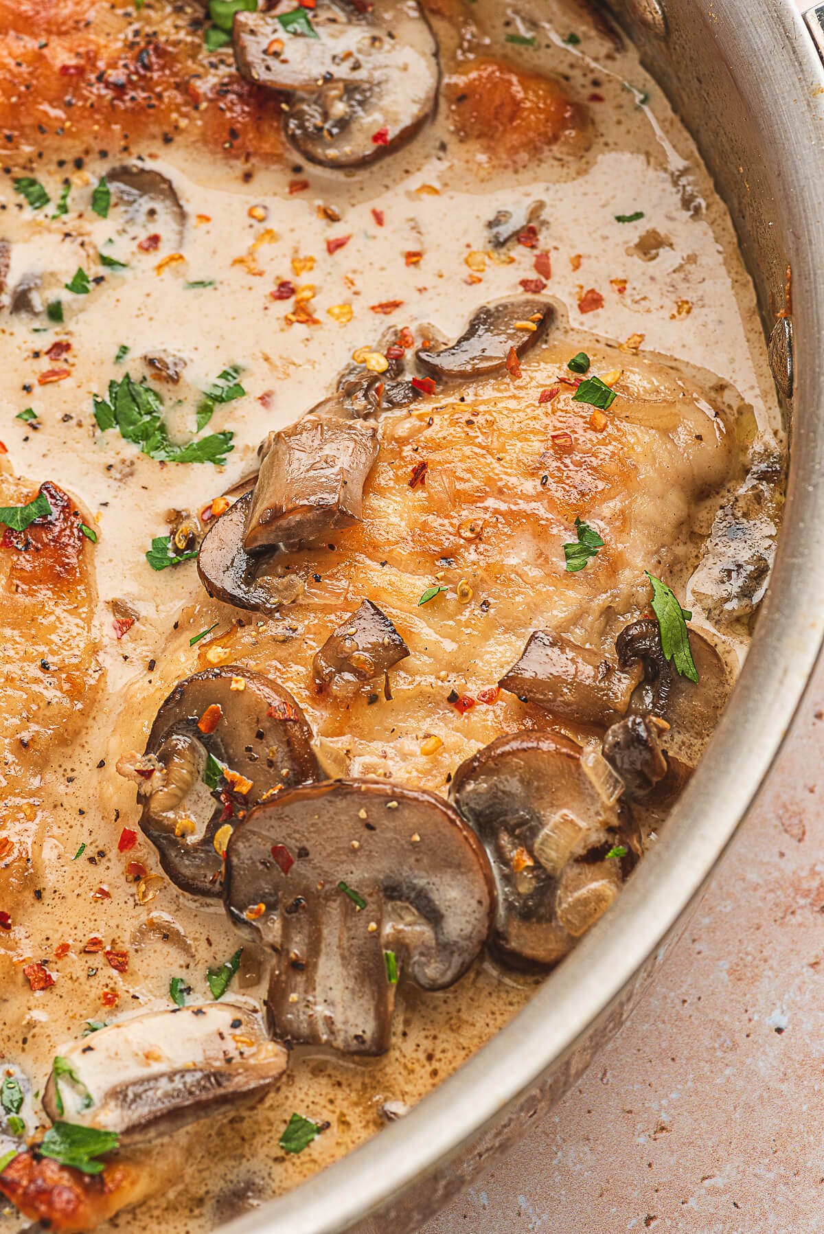 A cooked chicken breast and mushrooms swimming in a saucepan of creamy marsala sauce.
