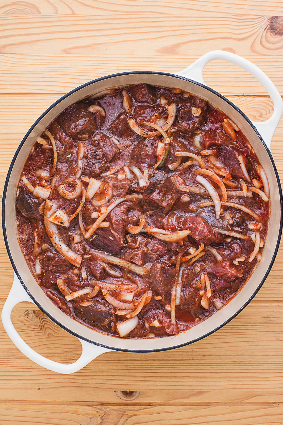 A Dutch oven filled with raw wild meat goulash in a tomato and onion sauce.