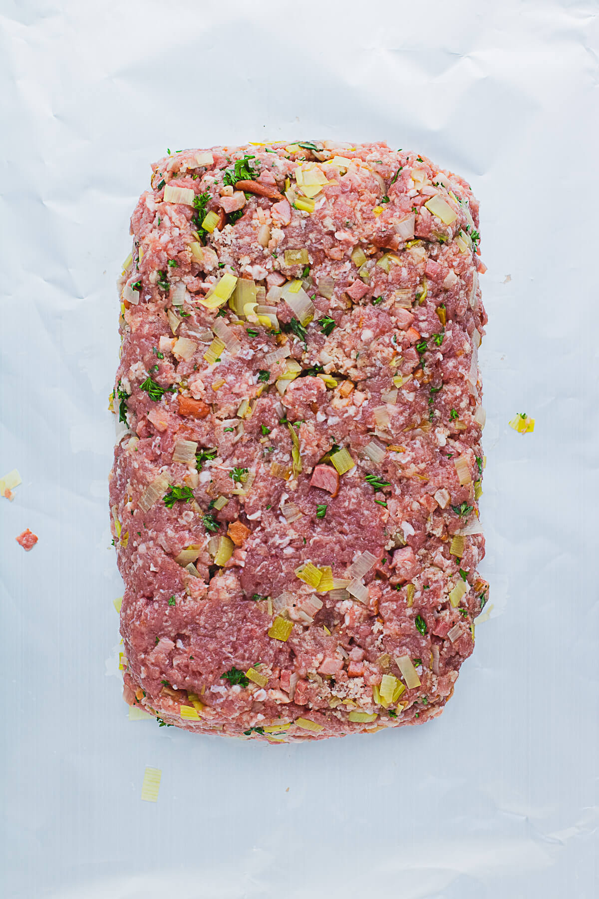 A raw free formed Pork meatloaf on a sheet of aluminium foil.